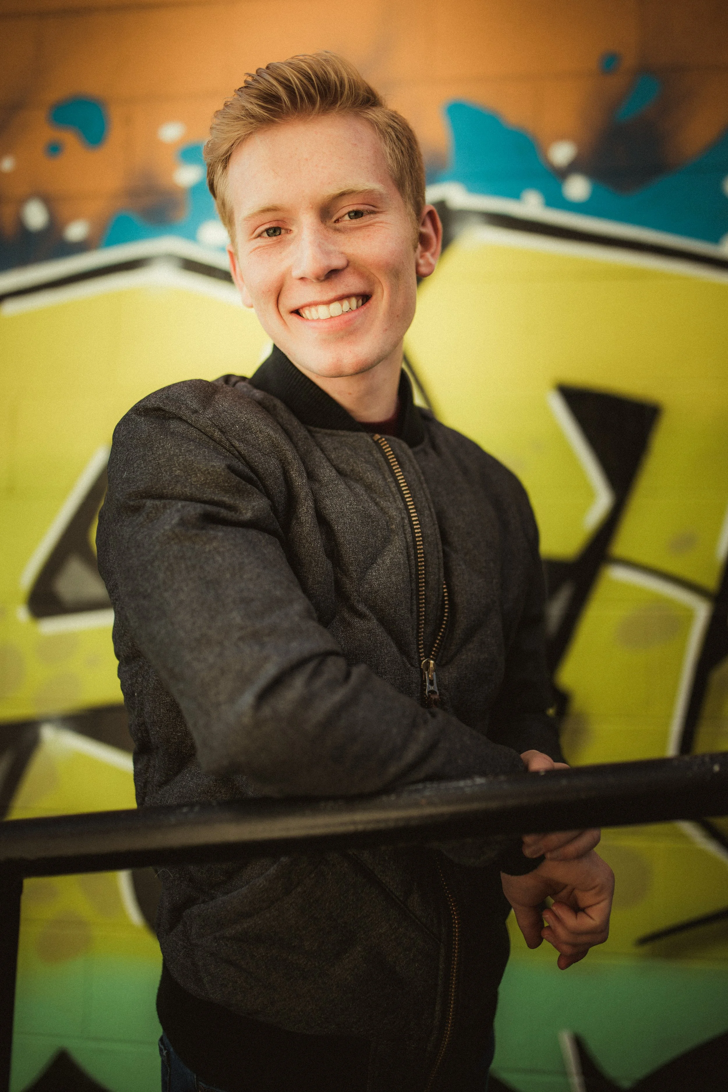A young man smiling and posing for the camera in front of colorful graffiti art.