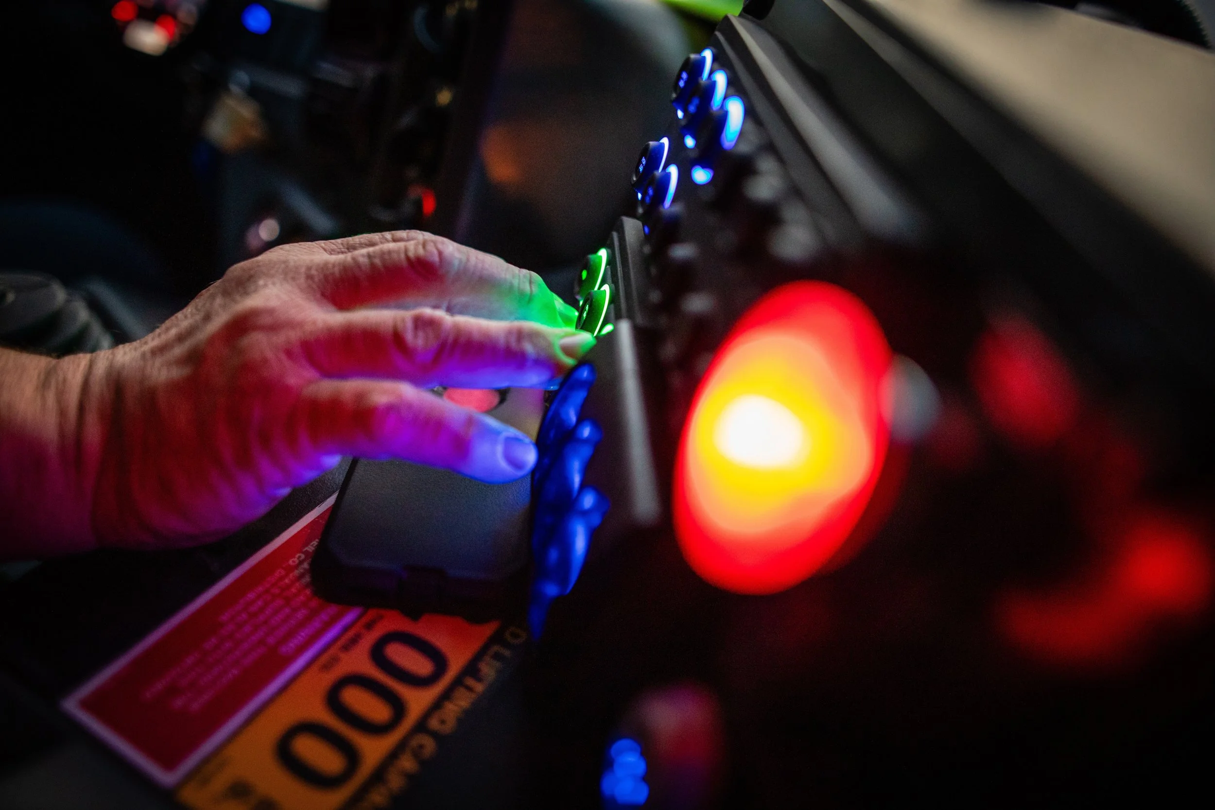 Close-up of a person's hand touching a colorful digital control panel with blue and green lights, with a red and yellow indicator light in the foreground.