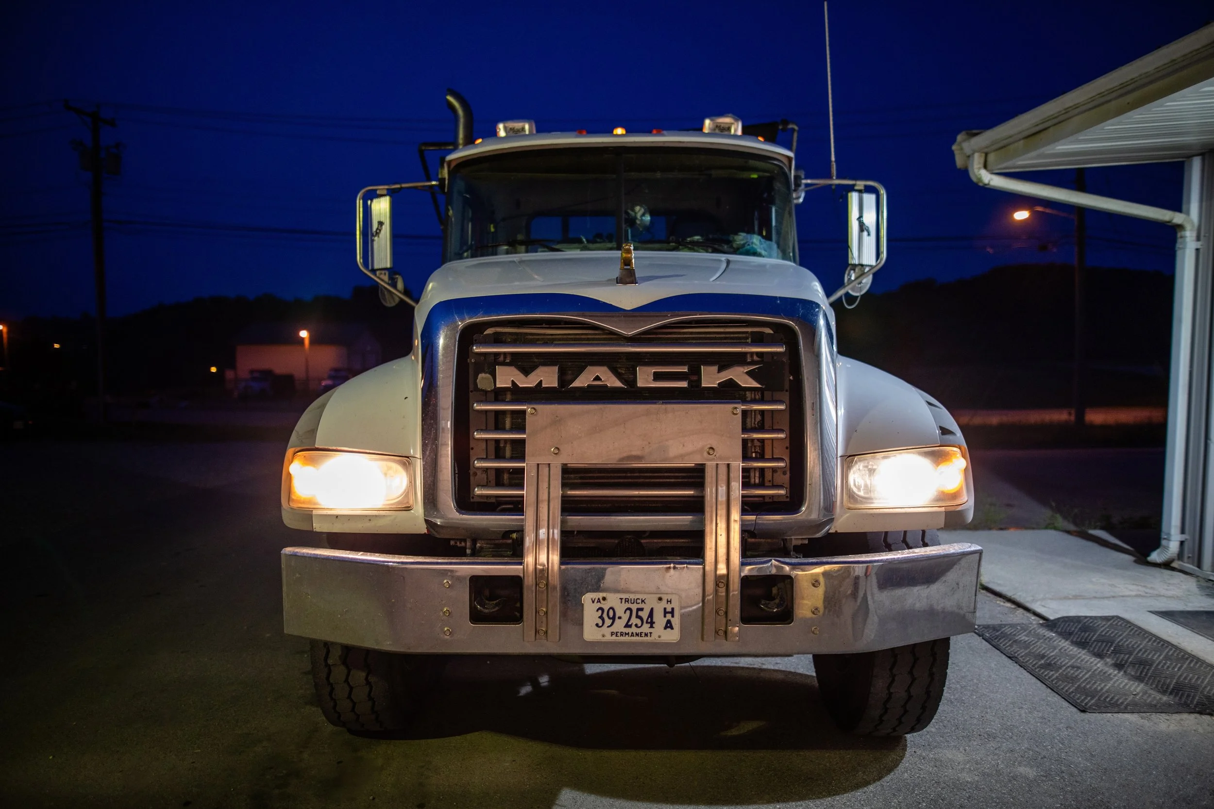 Front view of a Mack truck with headlights on parked outside during the night.
