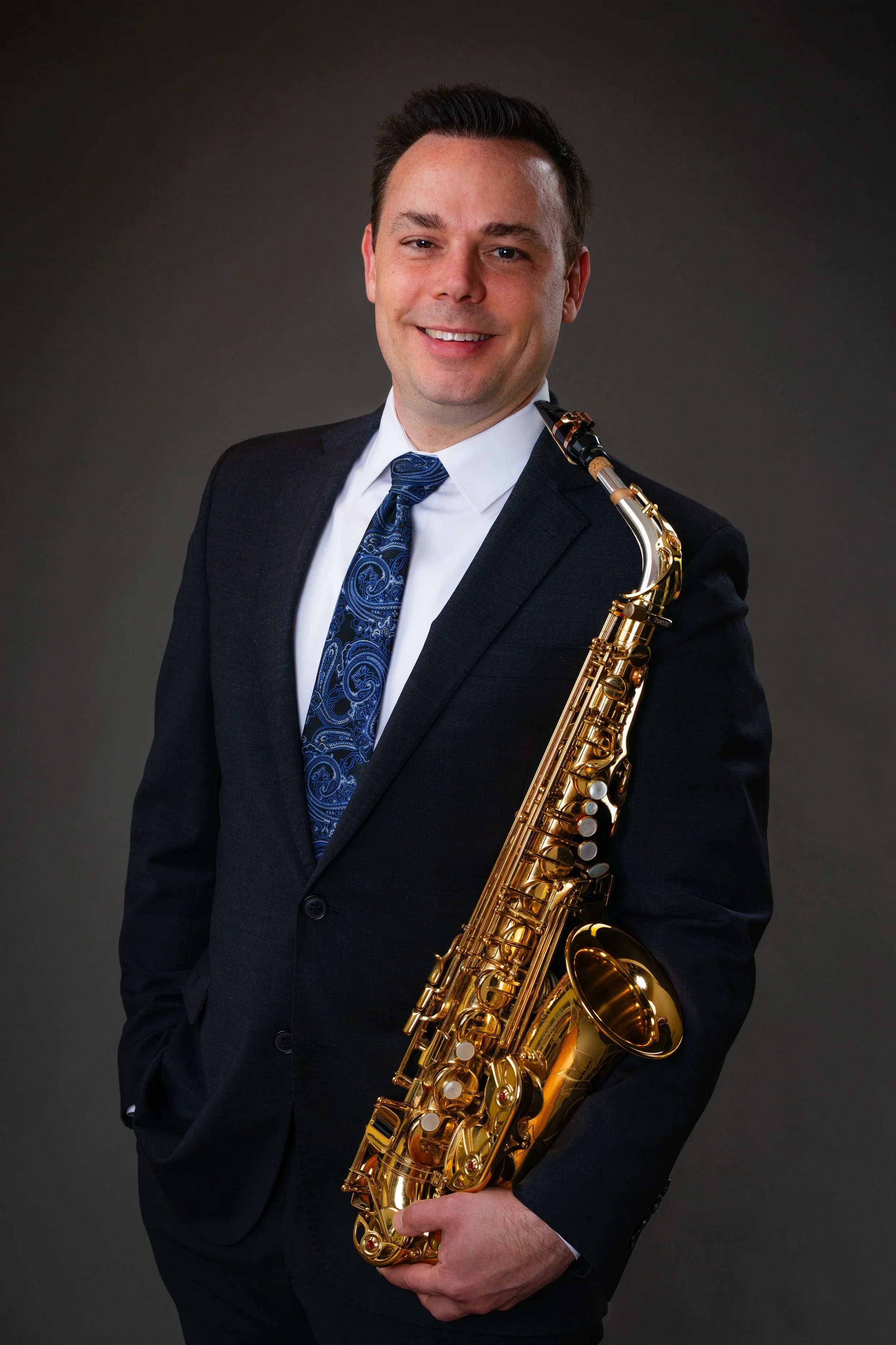 A man in a dark suit holding a gold saxophone.