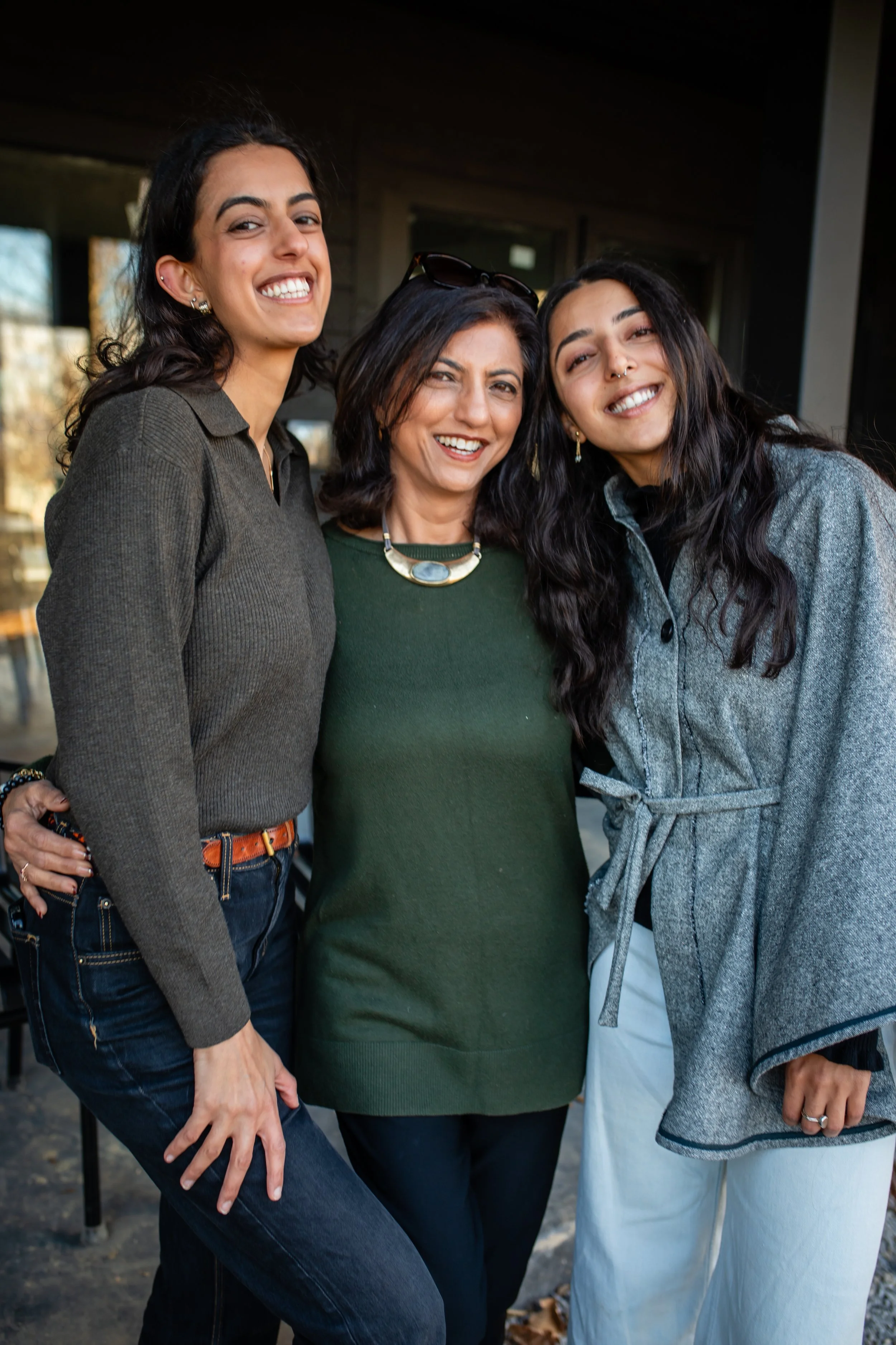 Three women standing close together outdoors, smiling at the camera.