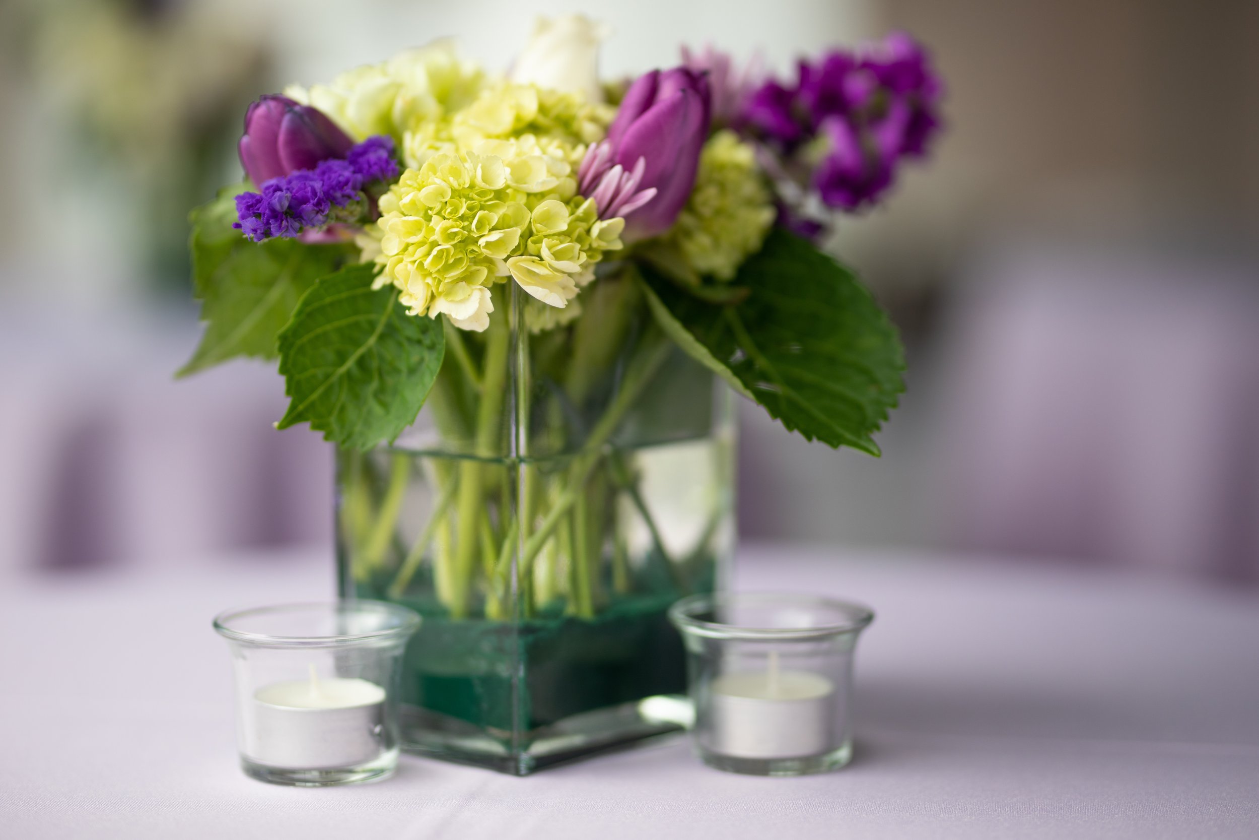 Colorful flower arrangement in a square glass vase on a table with two small tealight candles in glass holders