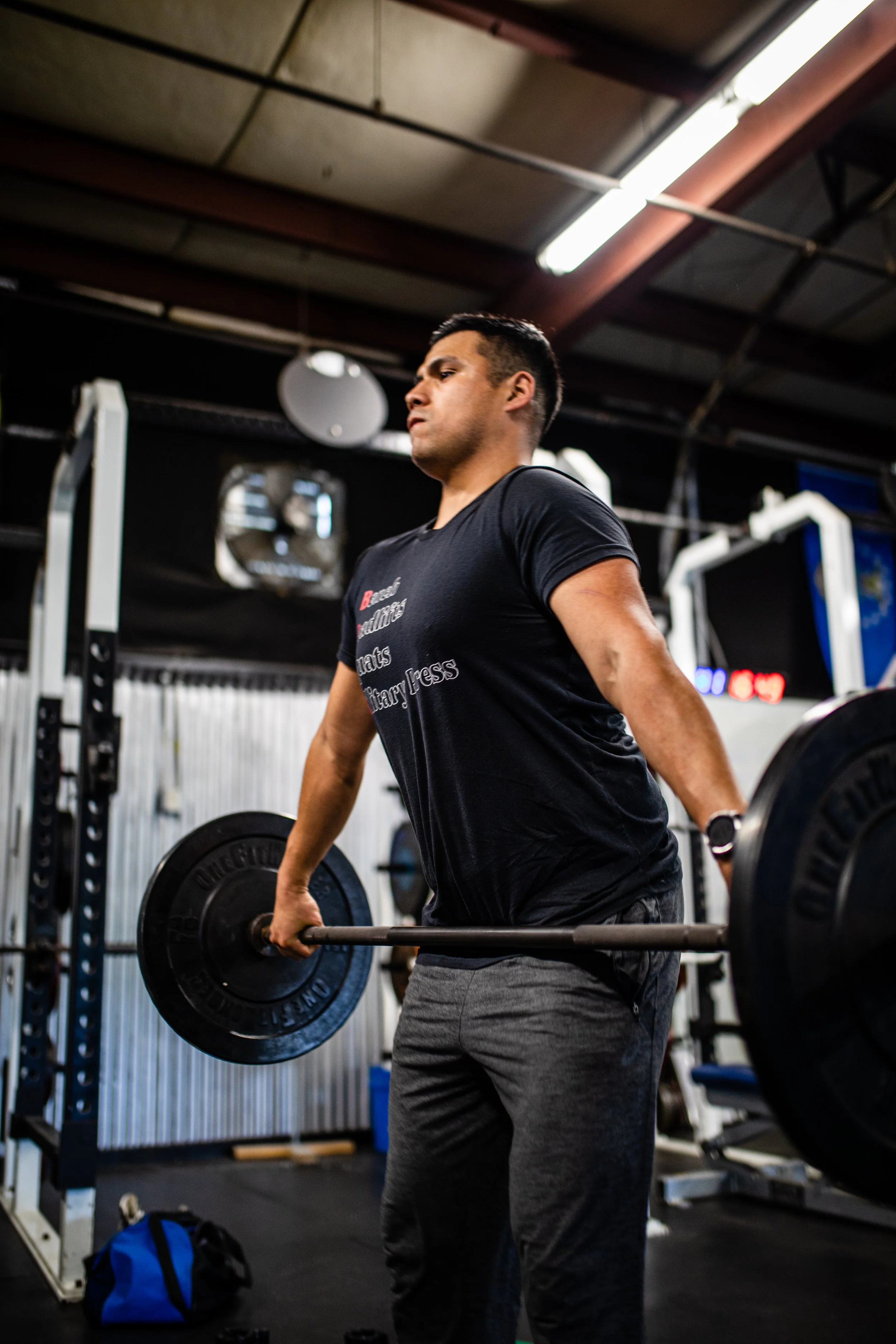 A man in a black t-shirt and gray sweatpants lifting a barbell in a gym.