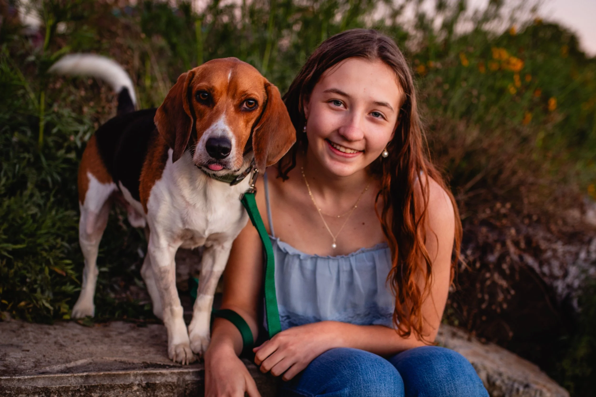 A young woman with long red hair and a bangle bracelet sitting outdoors with a beagle dog, both smiling.