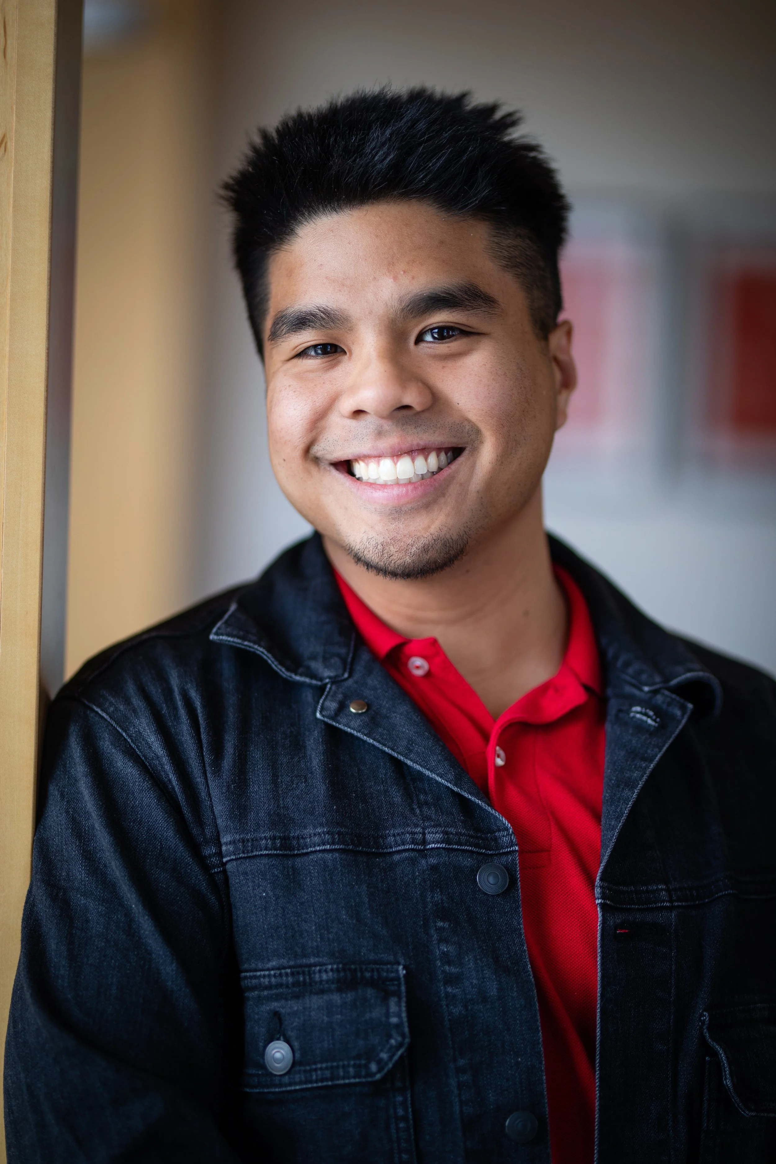 Portrait of a smiling young man leaning against a wall in an indoor setting.
