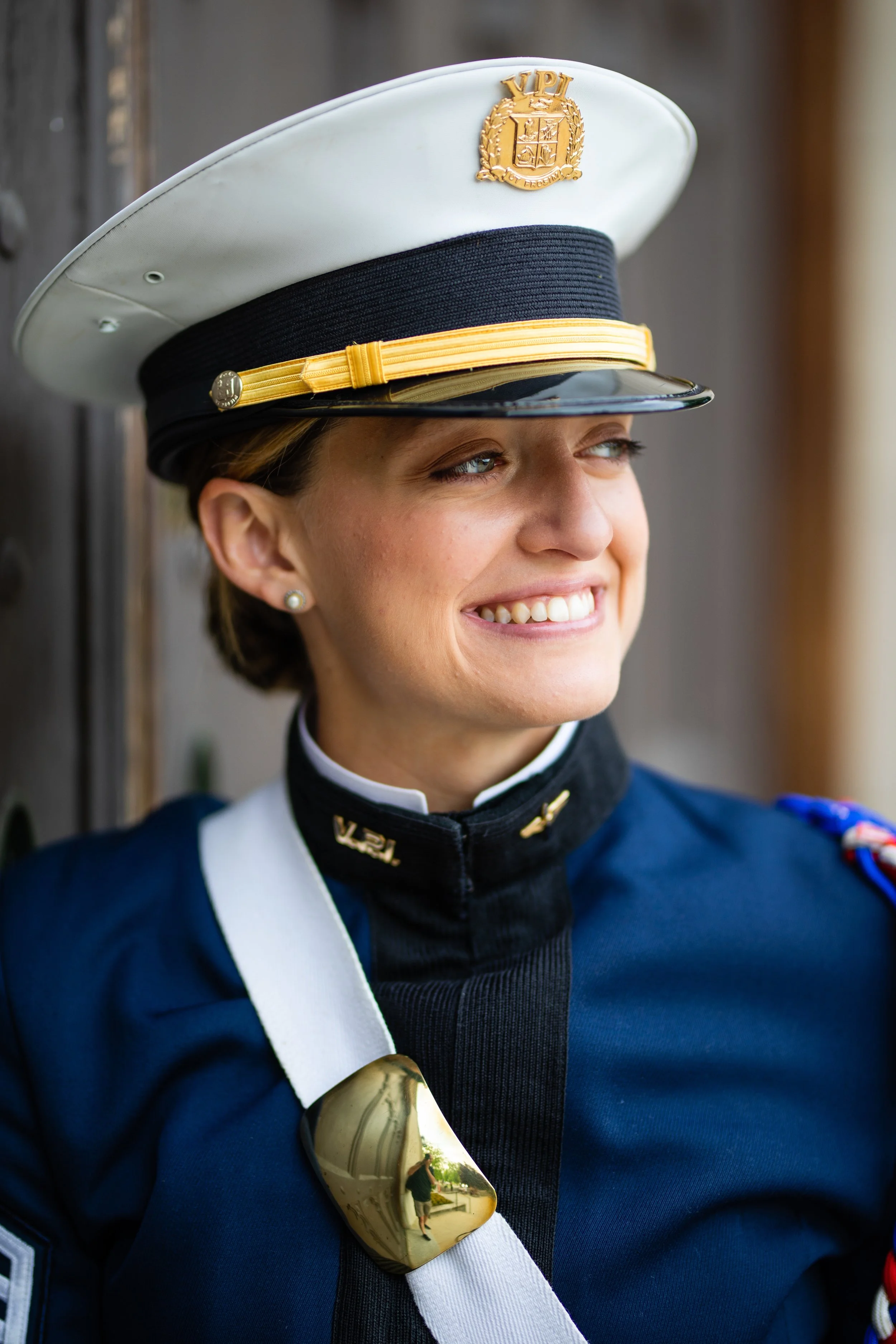A woman in a military uniform smiling, wearing a white military cap with gold emblem and a navy blue uniform with medals.