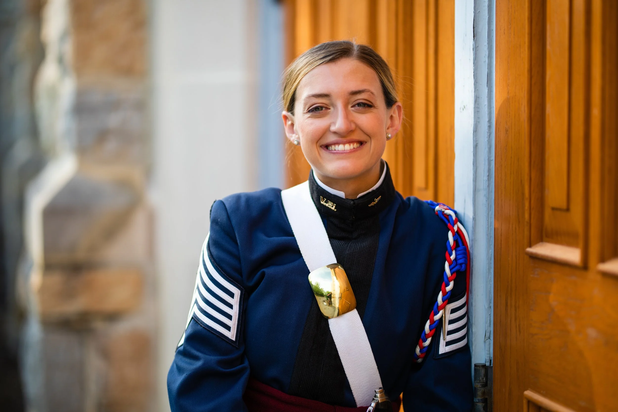A woman in a blue marching band uniform smiling and leaning against a wooden door.