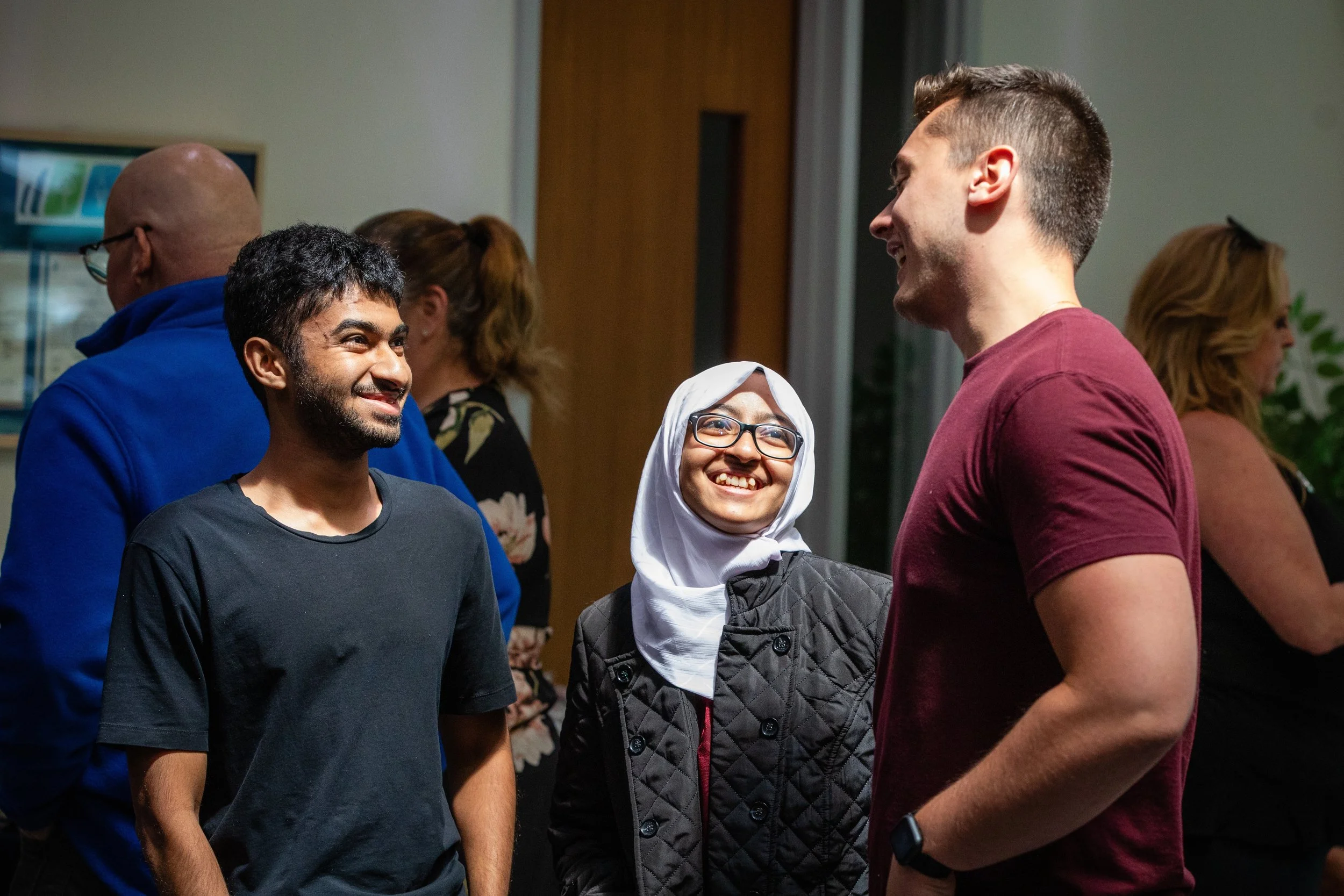 Three people smiling and talking at a social gathering, with two women and a man.
