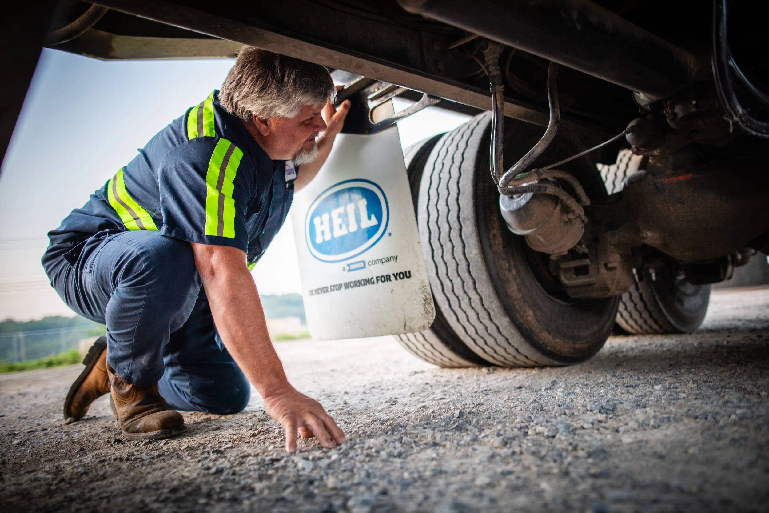 A man wearing work clothes inspecting the underside of a large truck.