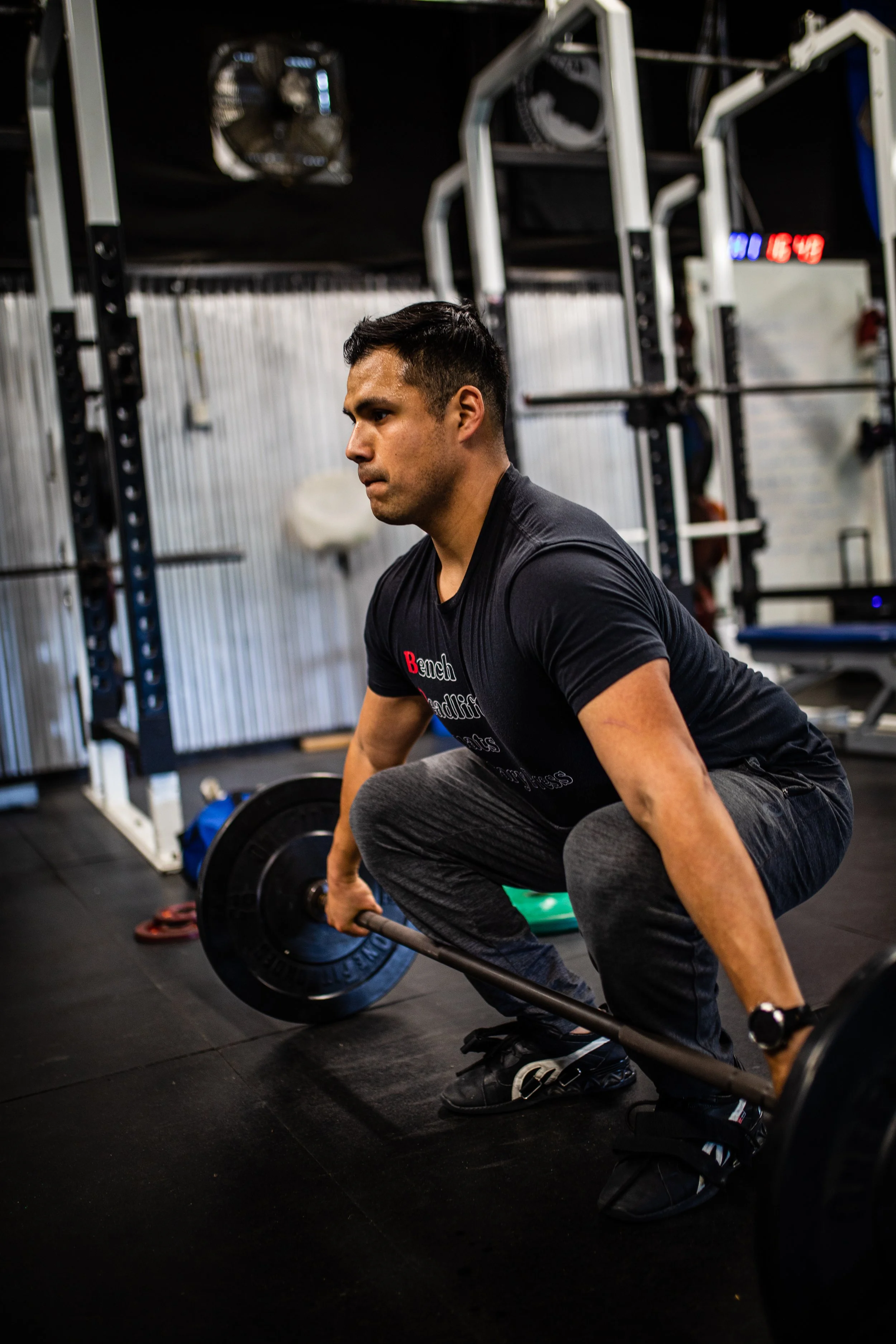 A man lifting a barbell in a gym, squatting.