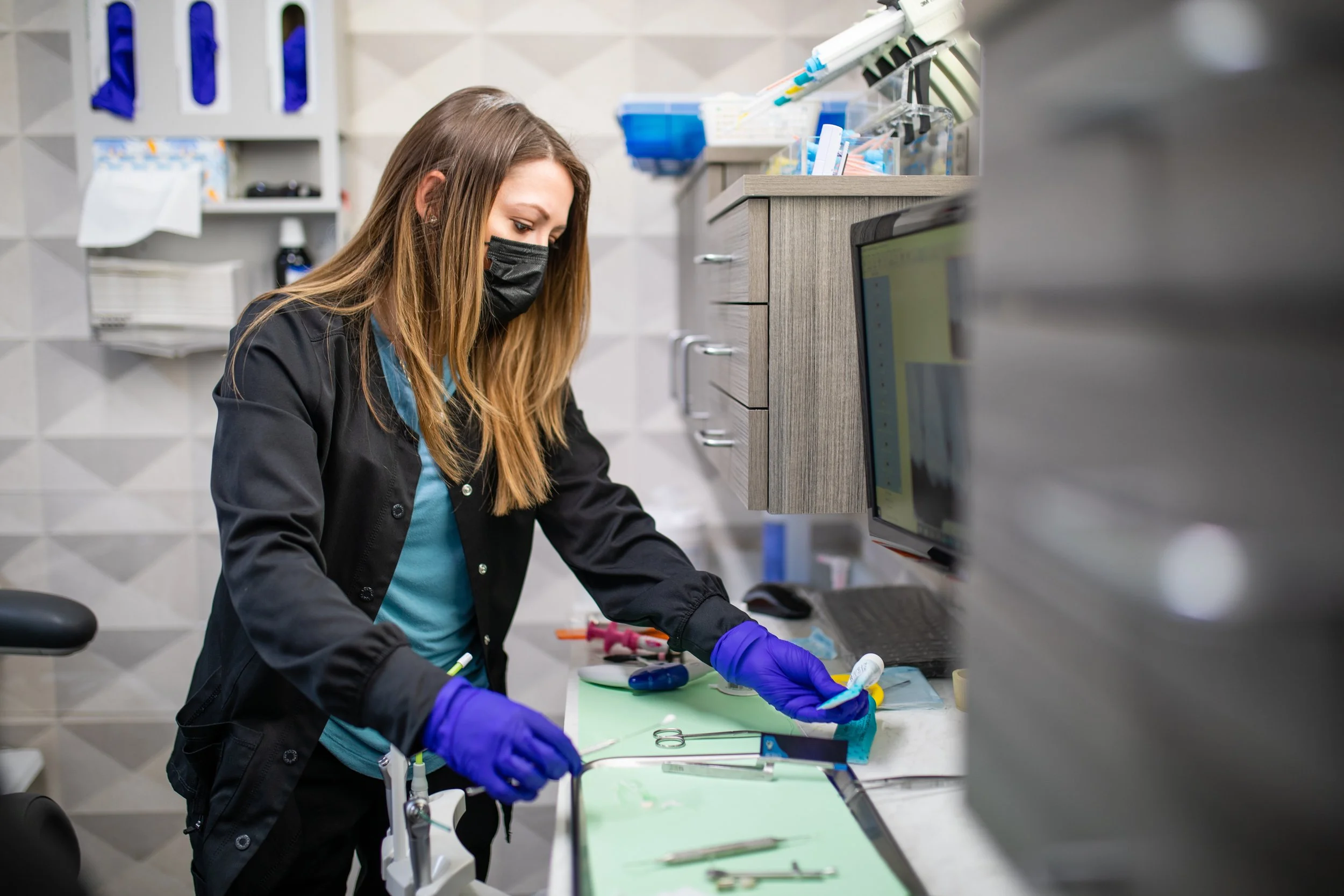 A female scientist wearing a black mask and purple gloves working with medical tools on a green mat in a laboratory.