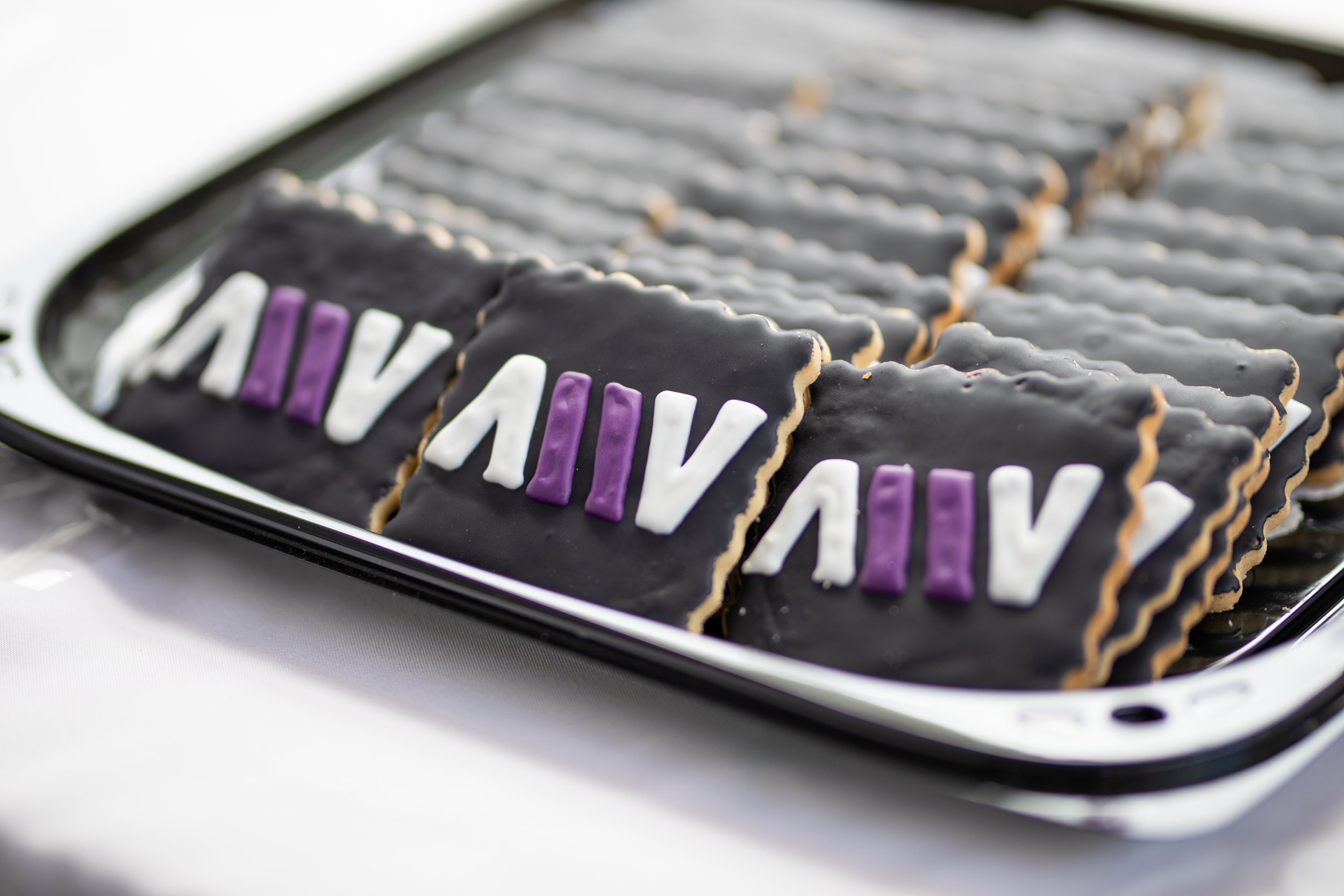 Tray of decorated cookies with the word 'Diversity' in purple, white, and black icing, arranged on a black tray.
