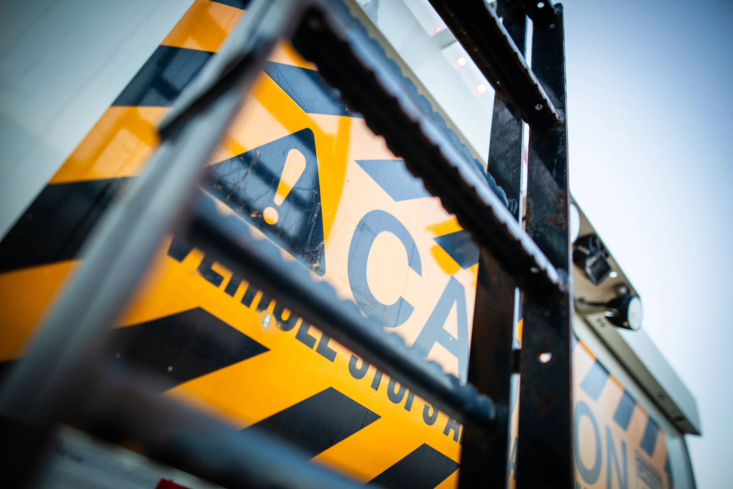 Close-up of a caution sign with yellow and black diagonal stripes, warning of possible danger, mounted on a structure with metal bars.