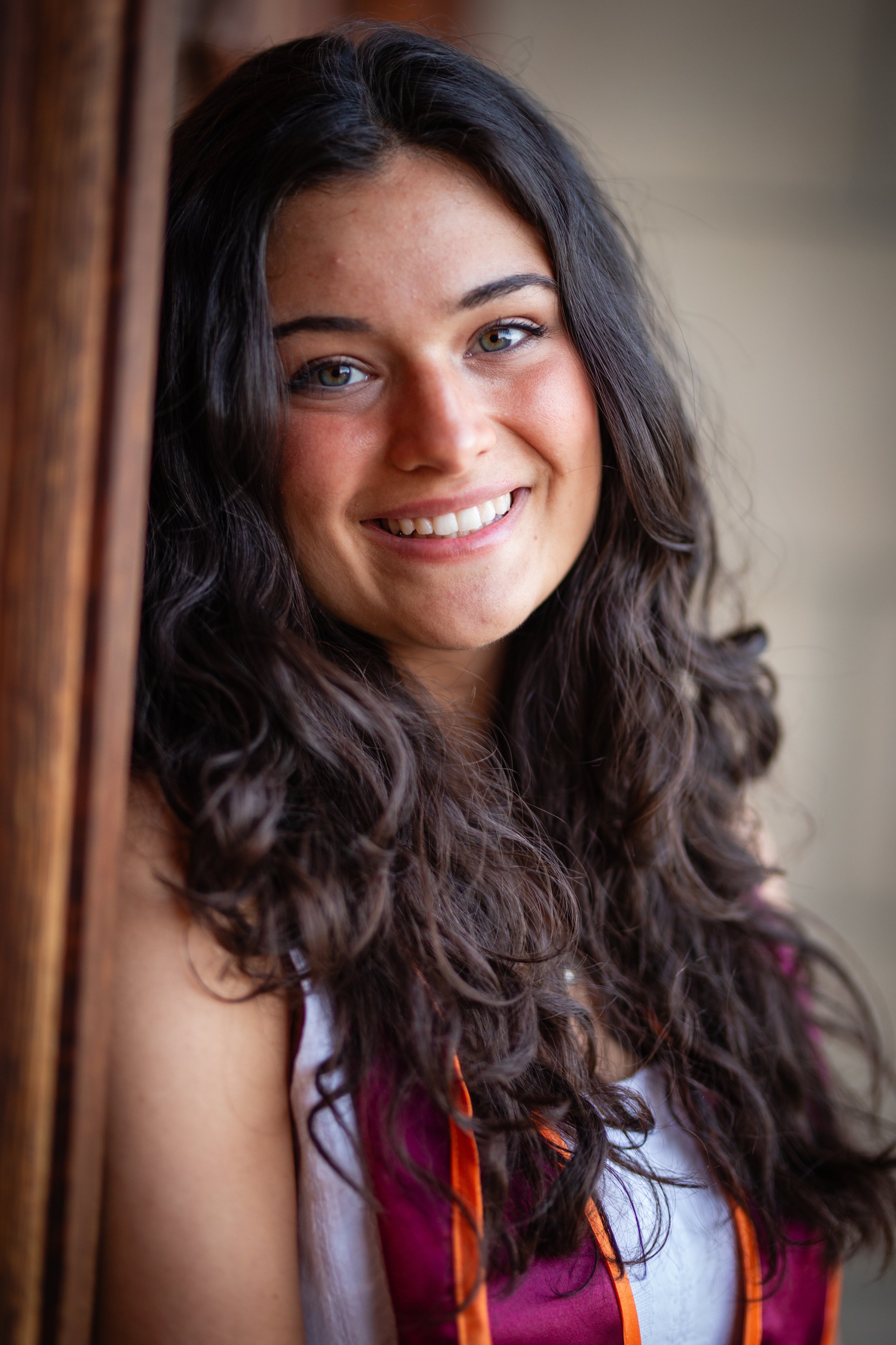 A young woman with long, dark curly hair smiling and looking at the camera.