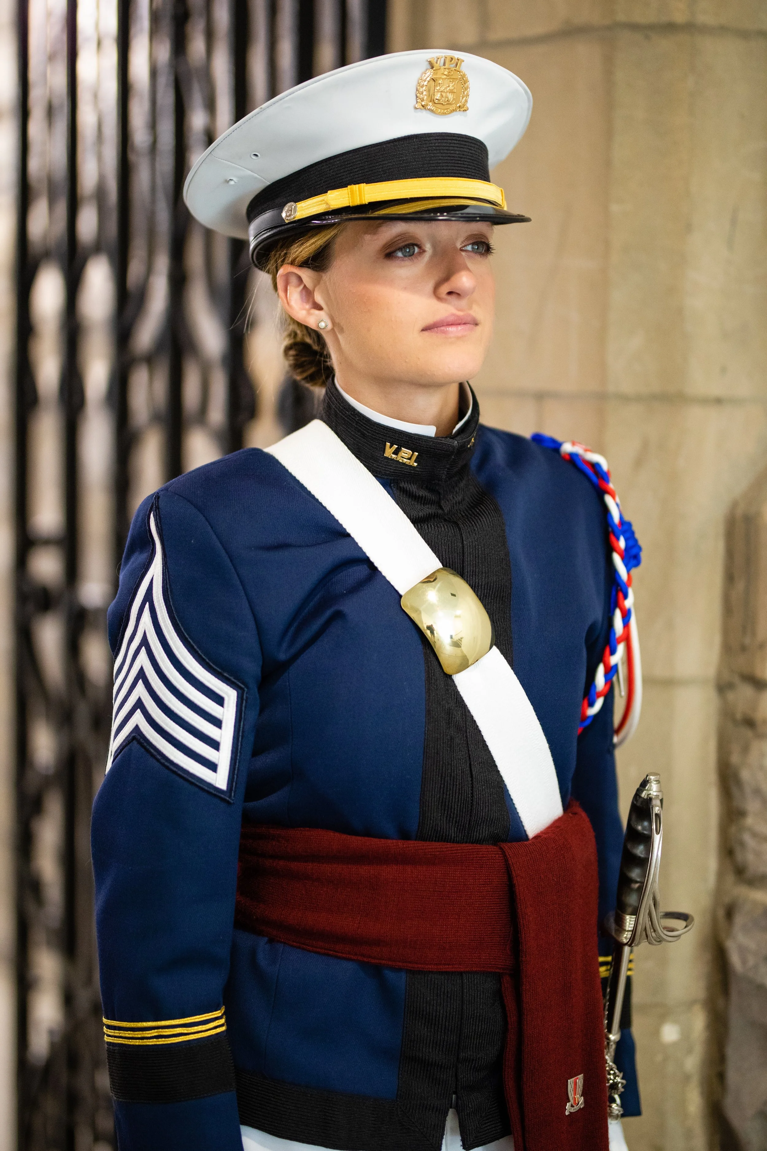 A woman dressed in a Spanish military uniform, wearing a white peaked cap with a gold emblem, a navy blue jacket with white and gold trim, and a red sash. She is standing indoors, possibly in a historical or ceremonial setting.