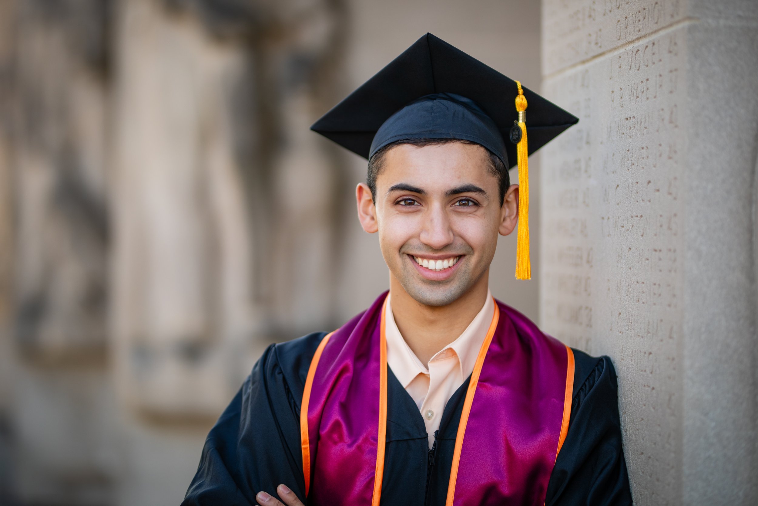Young man in graduation cap and gown smiling outdoors.