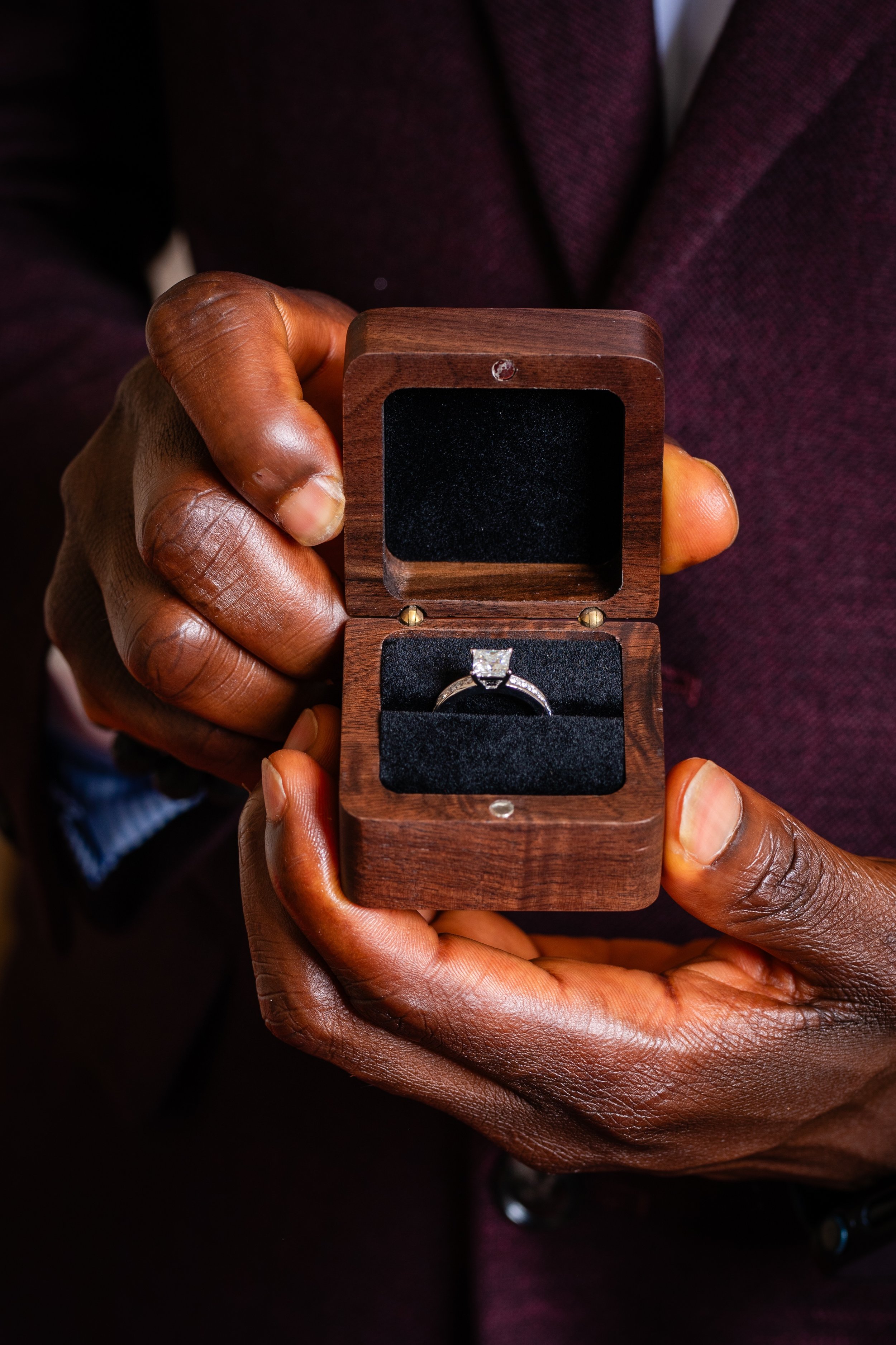 A person holding an open wooden jewelry box containing a diamond engagement ring.