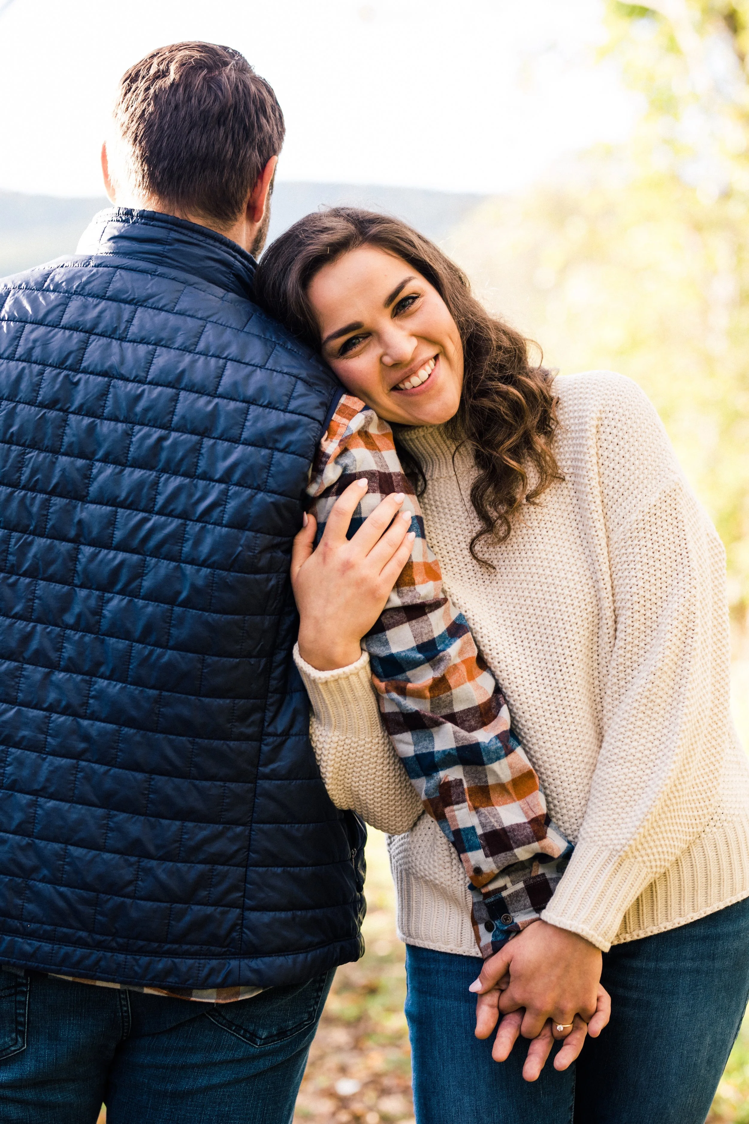 A couple sharing an intimate moment outdoors, with the woman smiling and holding hands, dressed in cozy fall clothing.