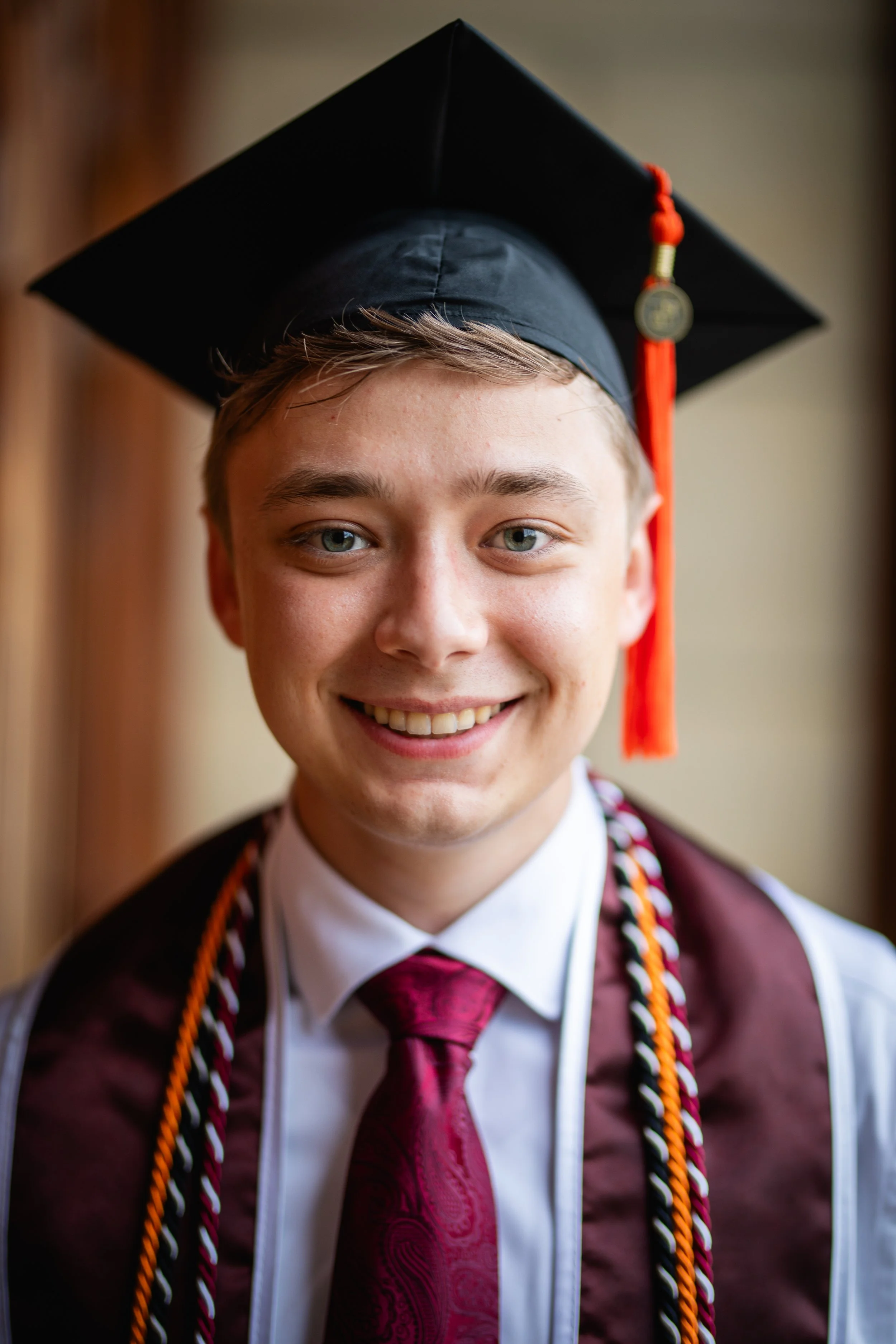Young man in a graduation cap and gown smiling at the camera.