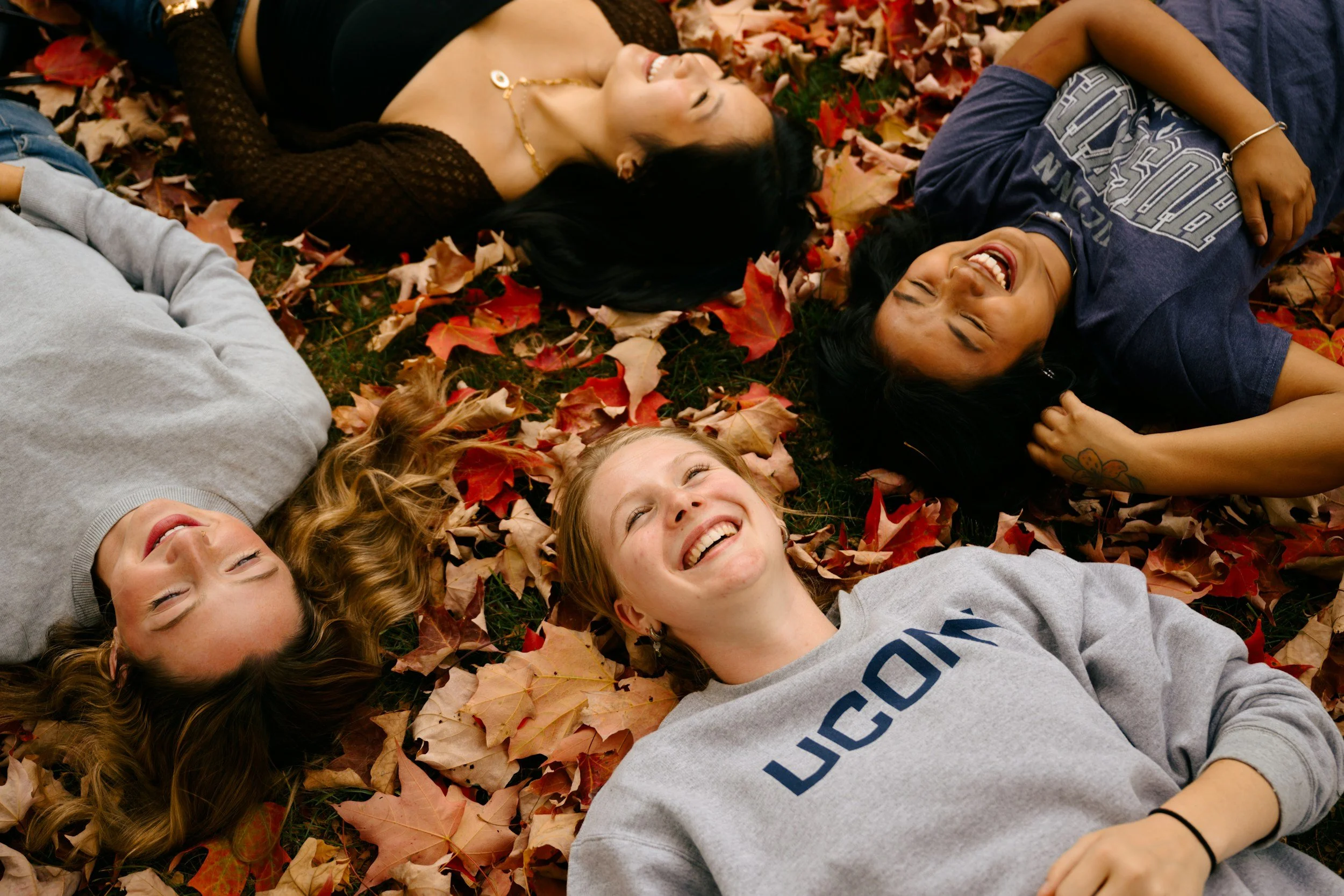 four friends hanging out and laughing in a bed of autumn leaves