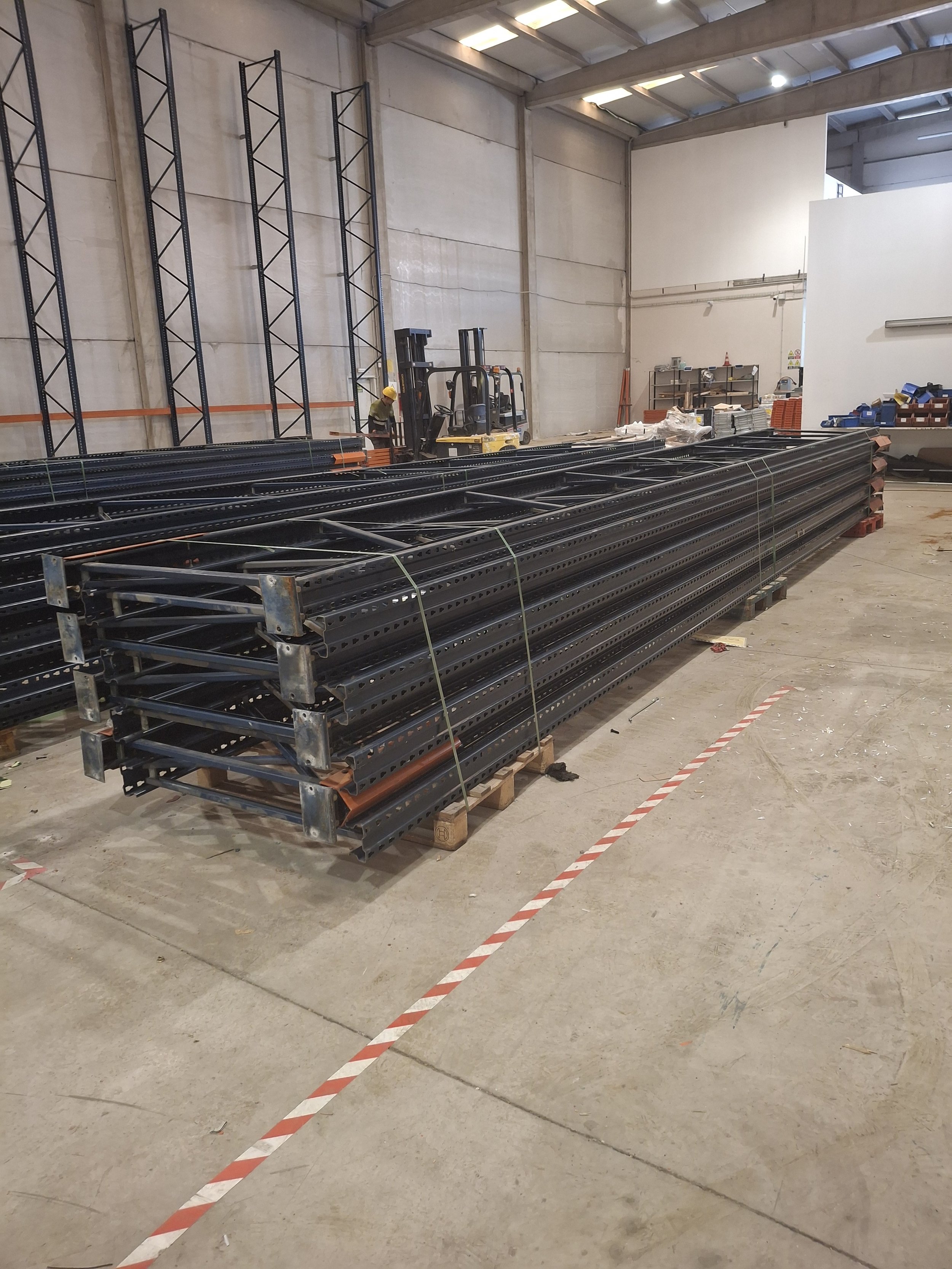 Interior de un almacén o fábrica en construcción con estanterías vacías, montacargas y materiales en el suelo.