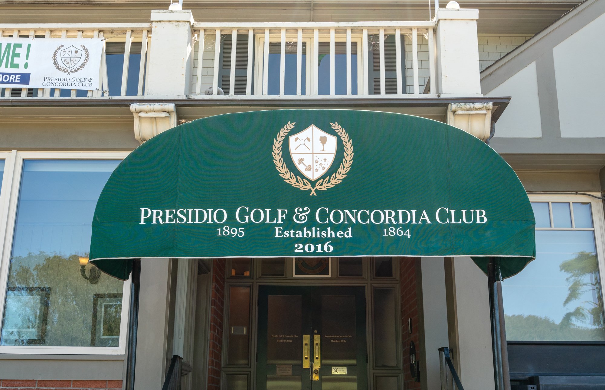 Green awning with gold emblem and white text that reads "Presidio Golf & Concordia Club 1895 Established 1864 2016" in front of a building entrance.