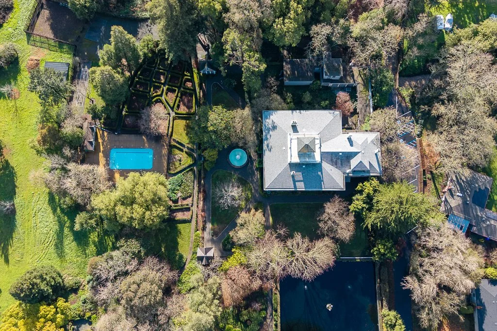 Aerial view of a large residential backyard with a house, swimming pool, garden, and surrounding trees.