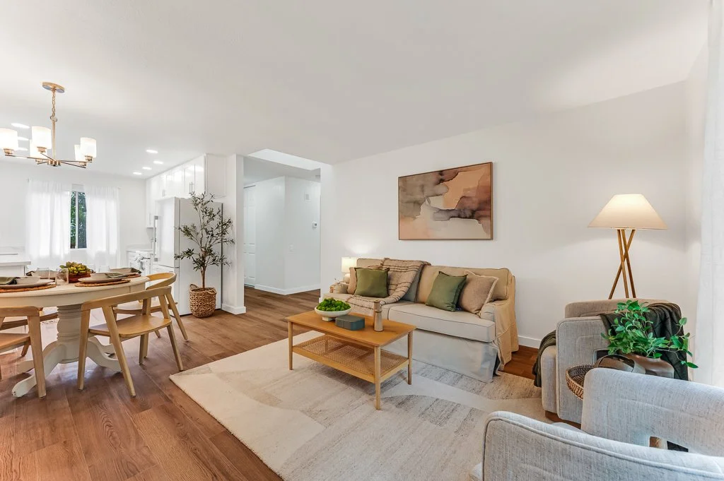 Open-concept living room and dining area with white walls, wooden floors, and neutral-colored furniture.