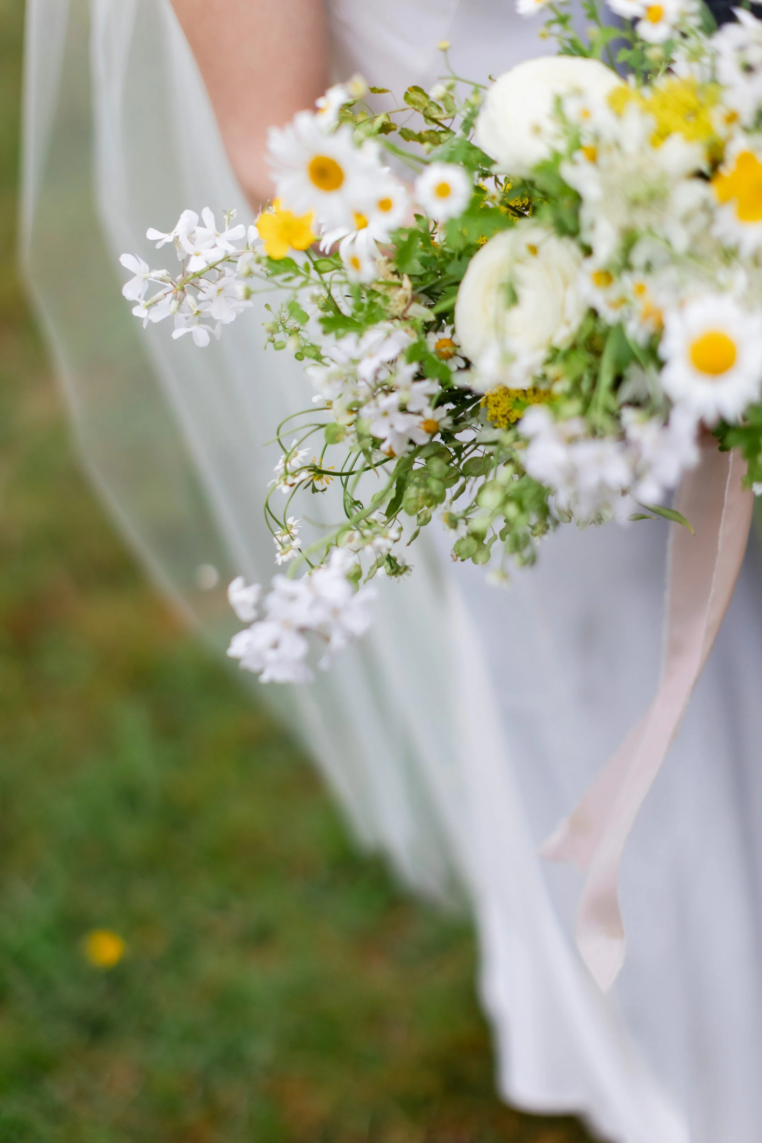 Close-up of a bouquet of white and yellow flowers held by a person wearing a white dress.
