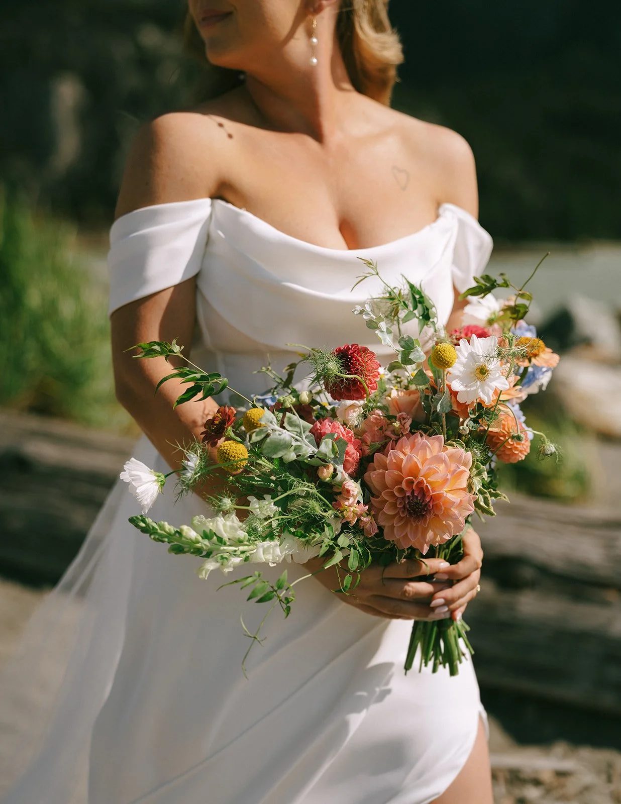 Woman in a white off-shoulder dress holding a bouquet of colorful flowers outdoors.