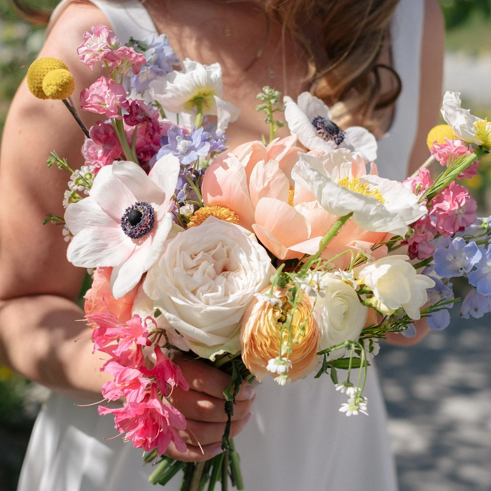 A woman holding a colorful bouquet of mixed flowers, including roses, anemones, and other blossoms, outdoors.