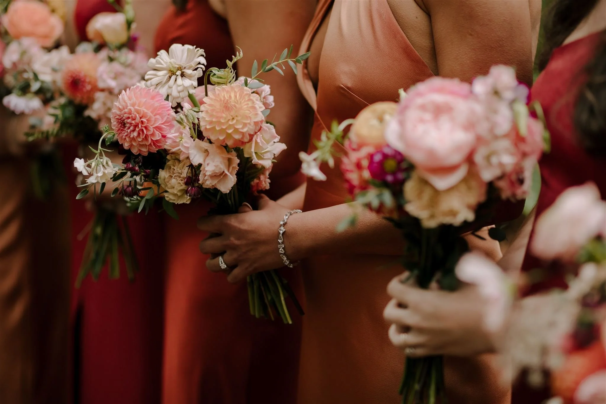 Close-up of bridesmaids holding bouquets of pink, peach, and cream-colored flowers at a wedding or outdoor event. Florist for weddings in Stroud, Wotton Under Edge, Bristol, Yate, Dursley, Tetbury, Malmesbury and Forest of Dean. 