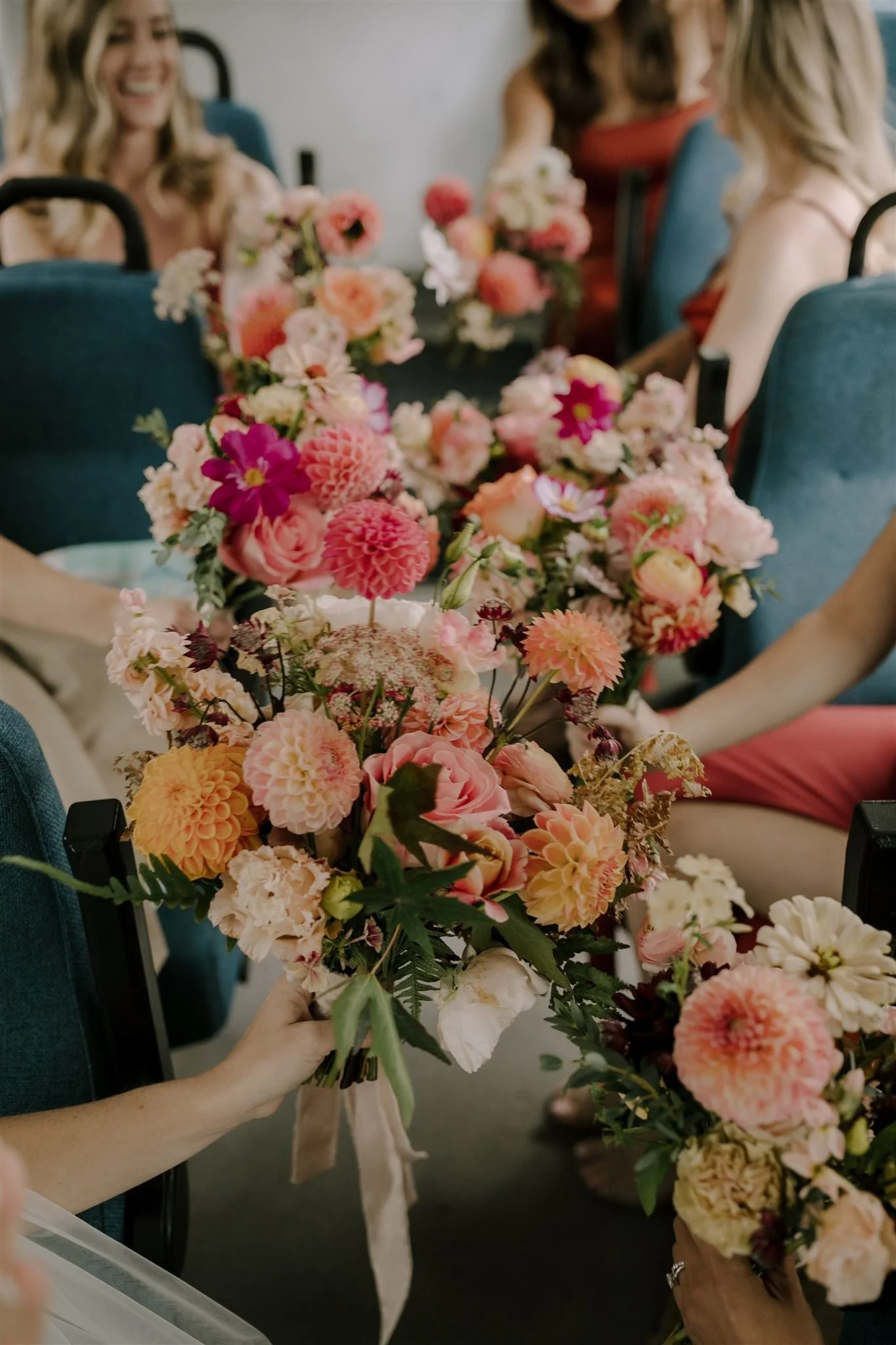 People participating in a flower arrangement activity, holding bouquets of colorful pink, peach, and white flowers with green leaves at a table. Florist for weddings in Stroud, Wotton Under Edge, Bristol, Yate, Dursley, Tetbury, Malmesbury and Forest