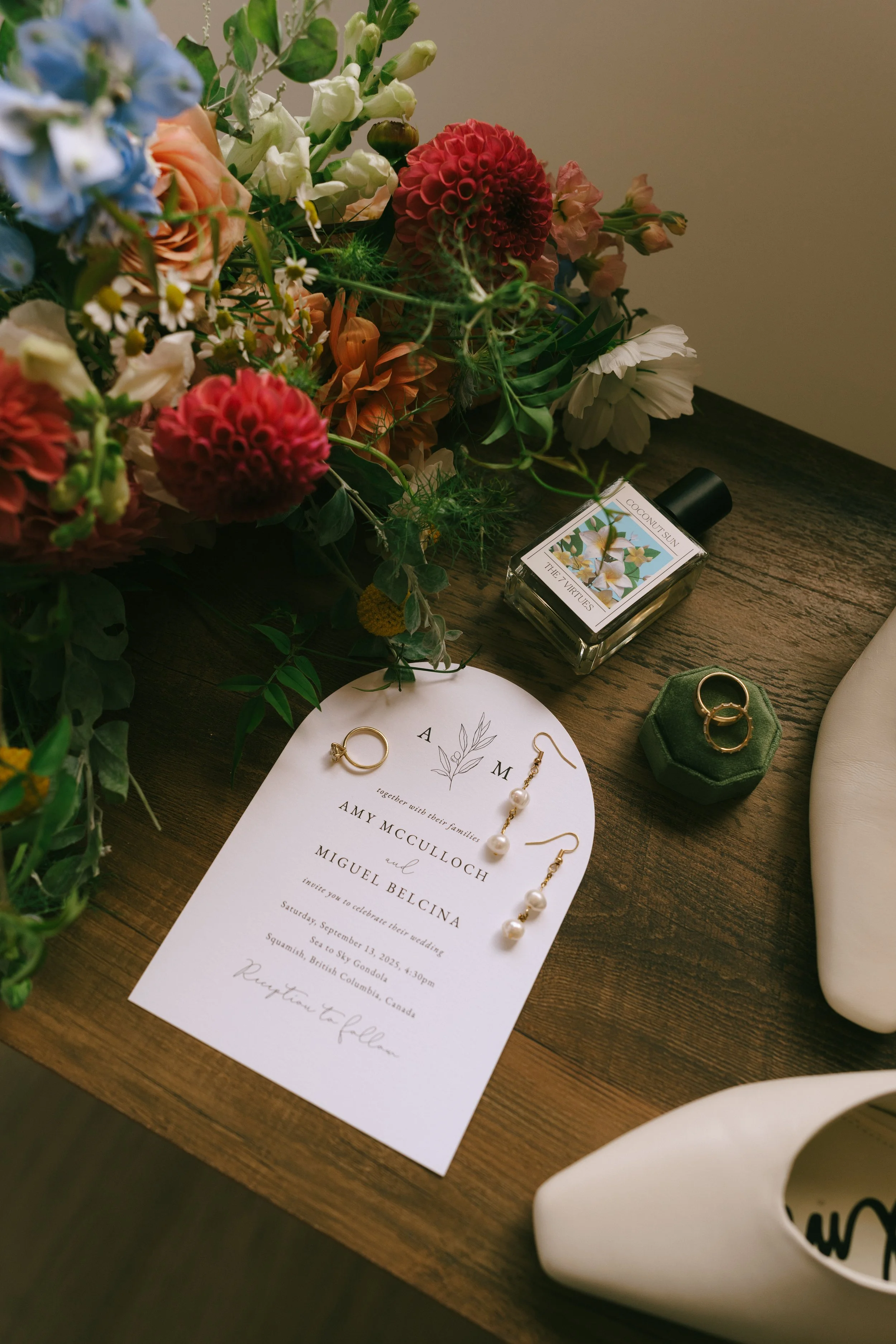 Wedding invitation surrounded by jewelry, flowers, a perfume bottle, and a shoe on a wooden table. Florist for weddings in Stroud, Wotton Under Edge, Bristol, Yate, Dursley, Tetbury, Malmesbury and Forest of Dean. 