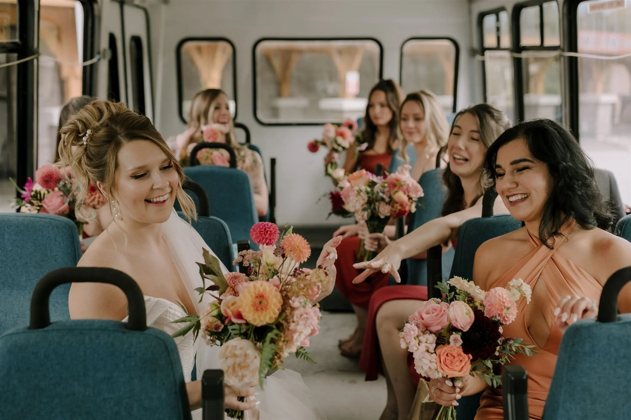 Bridesmaids dresses sitting on a bus, holding bouquets of flowers, laughing and smiling, celebrating wedding. Florist for weddings in Stroud, Wotton Under Edge, Bristol, Yate, Dursley, Tetbury, Malmesbury and Forest of Dean. 