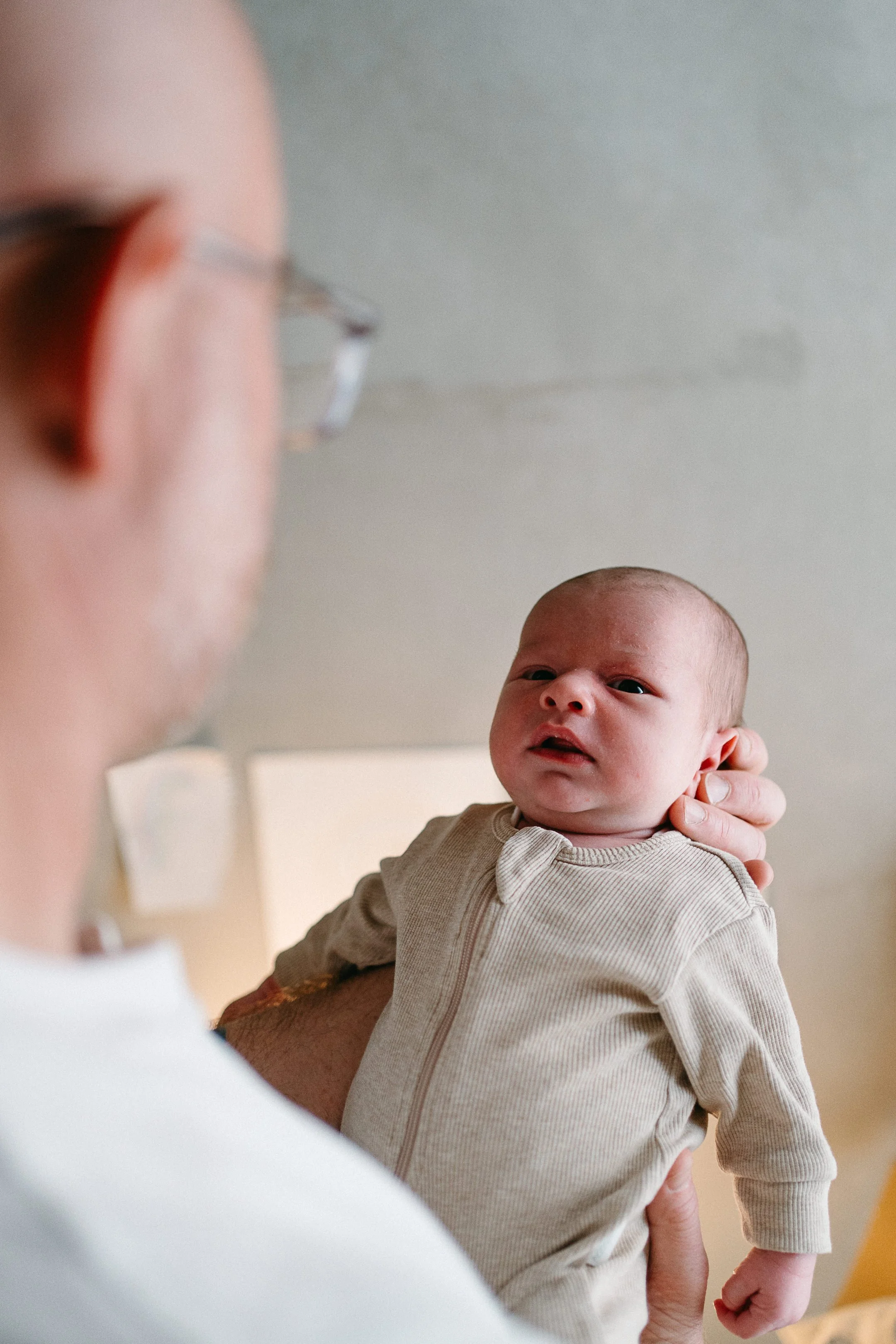 A baby being held up by an adult, looking at the adult with a curious expression.