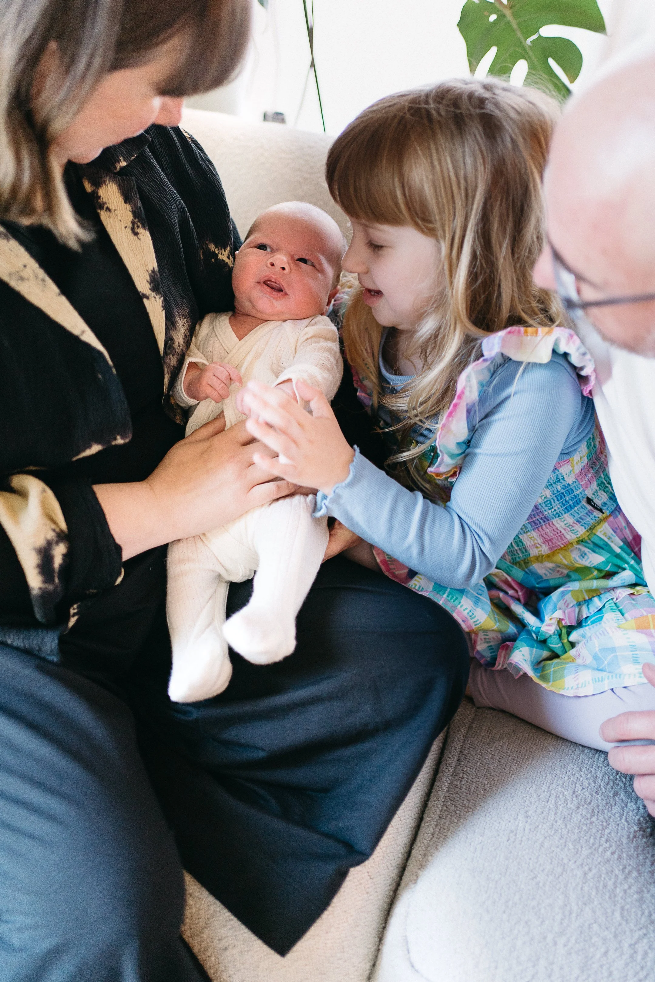 A baby being held by an adult, with a young girl and an older man nearby, all engaging in a moment of interaction.