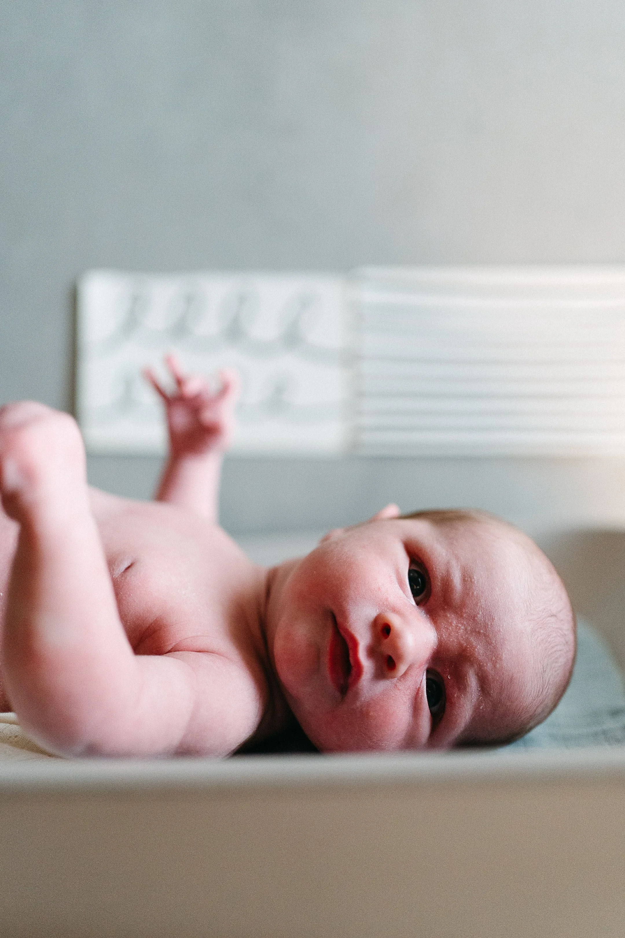 A newborn baby lying on a changing table looking at the camera with wide eyes.