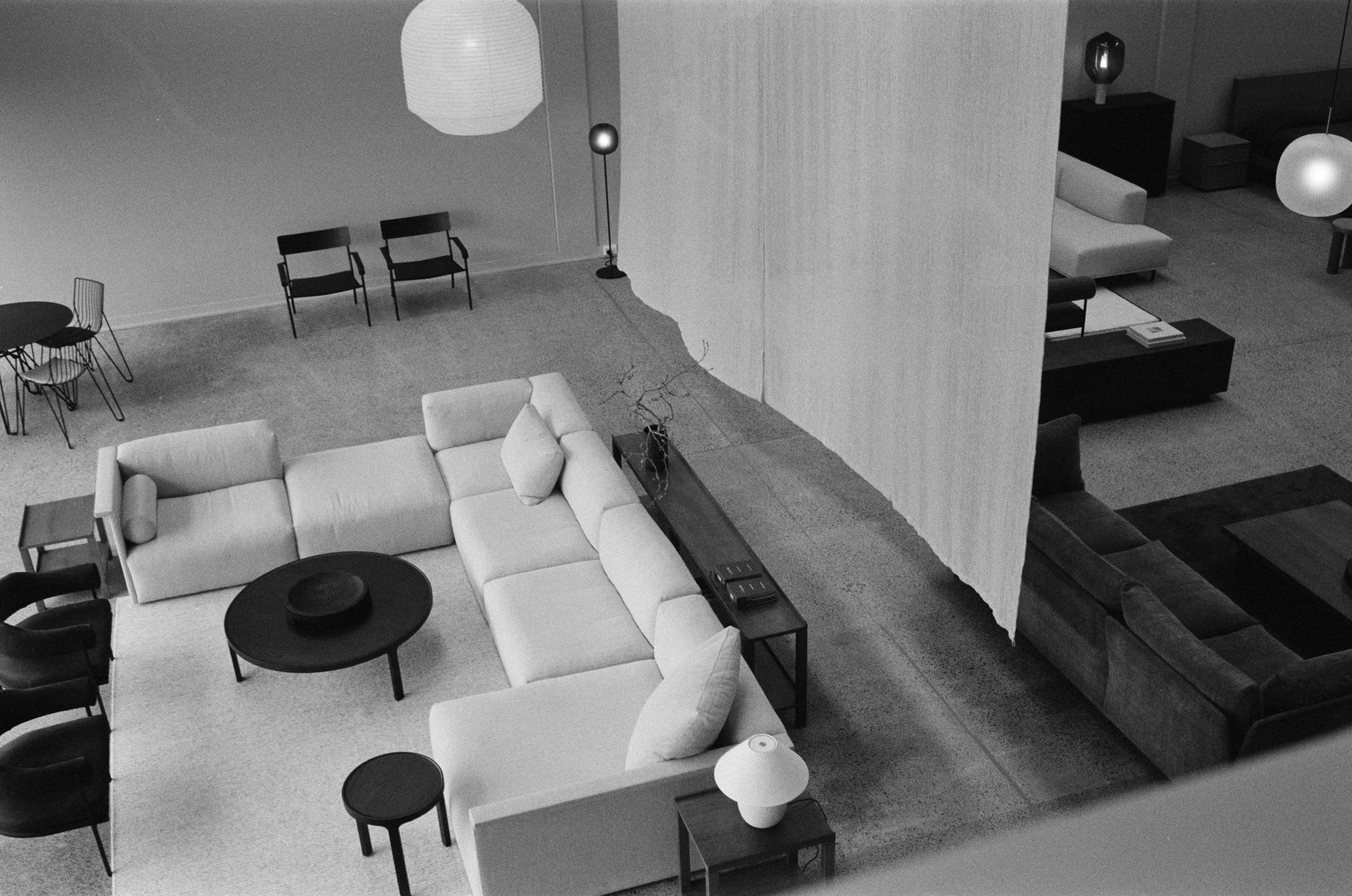 A top-down view of a modern furniture showroom with a sectional sofa, coffee tables, chairs, lamps, and decorative items in a black and white photo.
