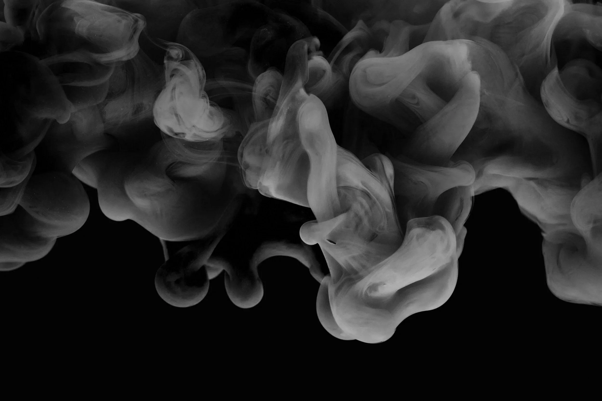 Black and white abstract smoke or ink swirling in water with a dark background.