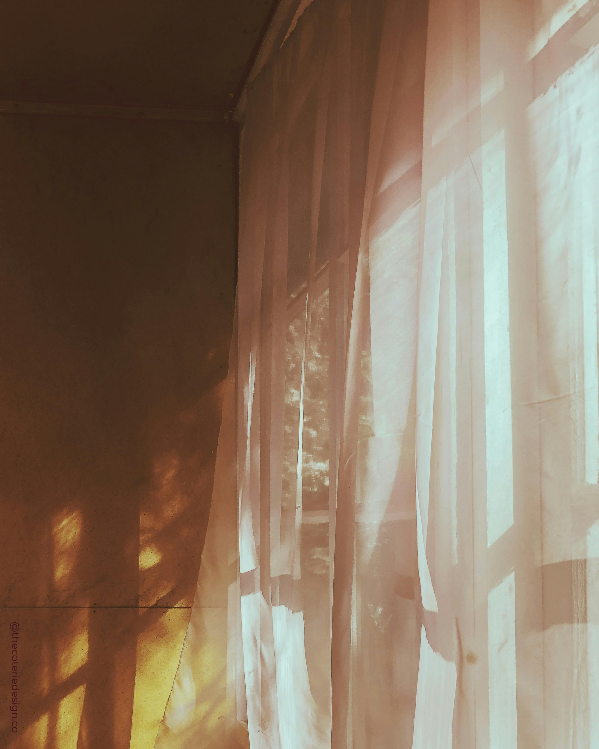 Sunlight streaming through white curtains onto a wooden floor in a softly lit room.