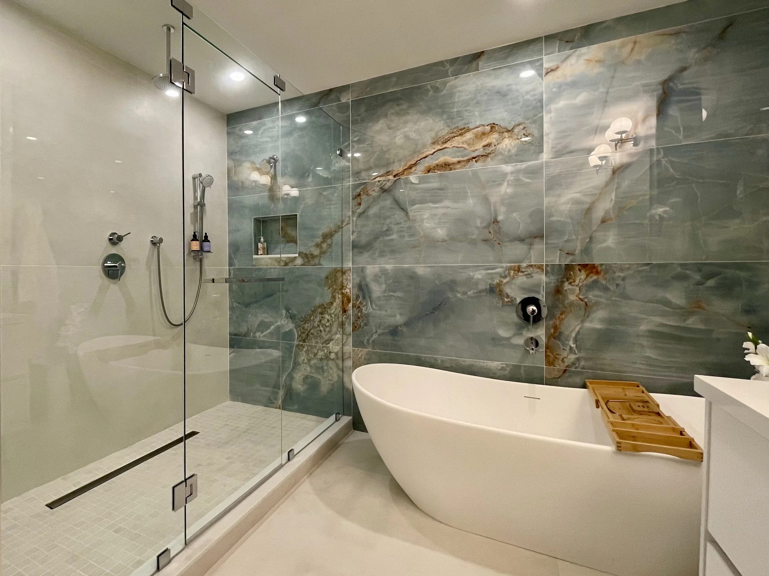Modern bathroom with a glass-enclosed shower, green marble wall, and a white freestanding bathtub.