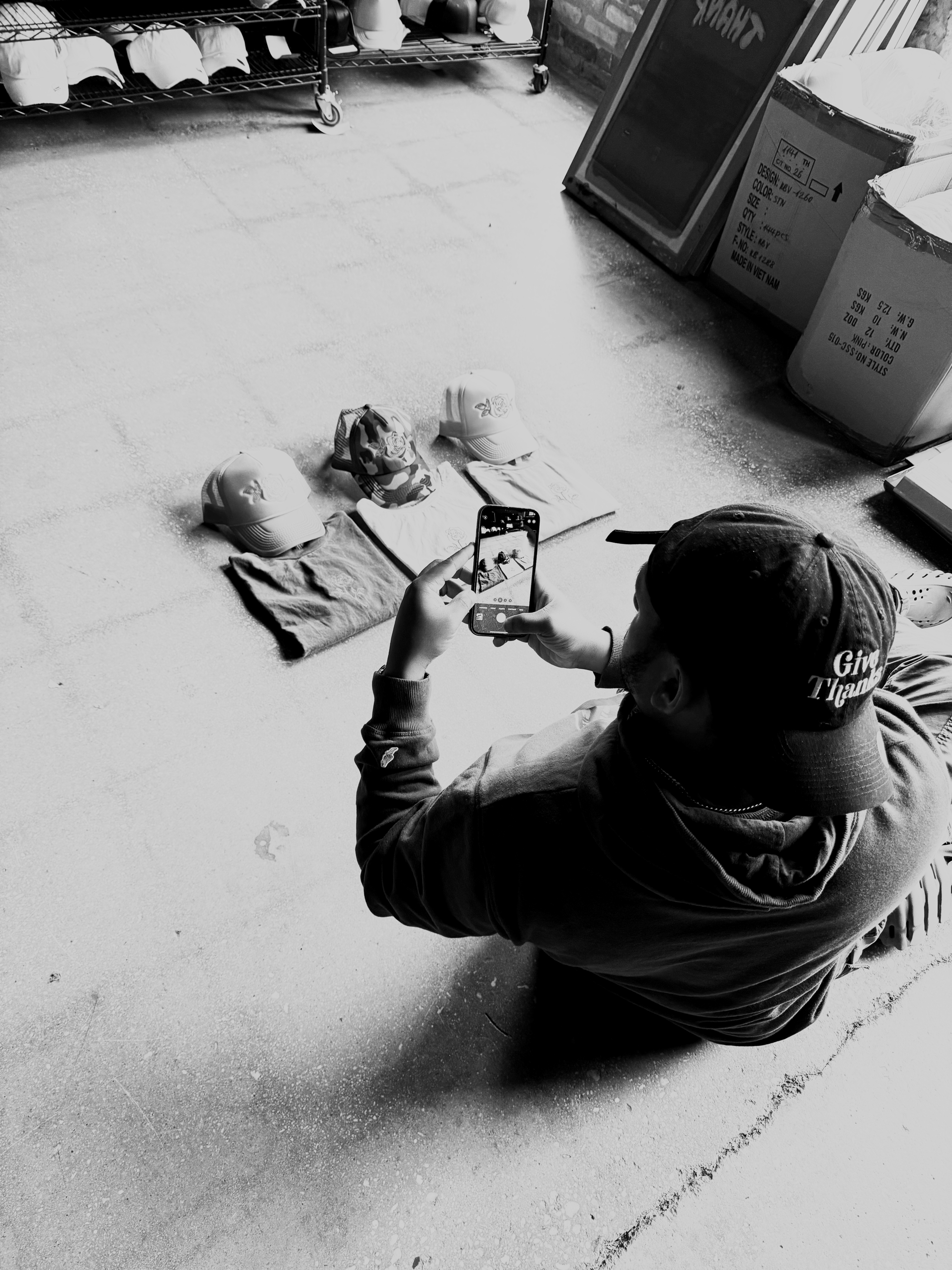 Person taking a photo with smartphone of hats and t-shirts laid out on the floor at a retail store or market.