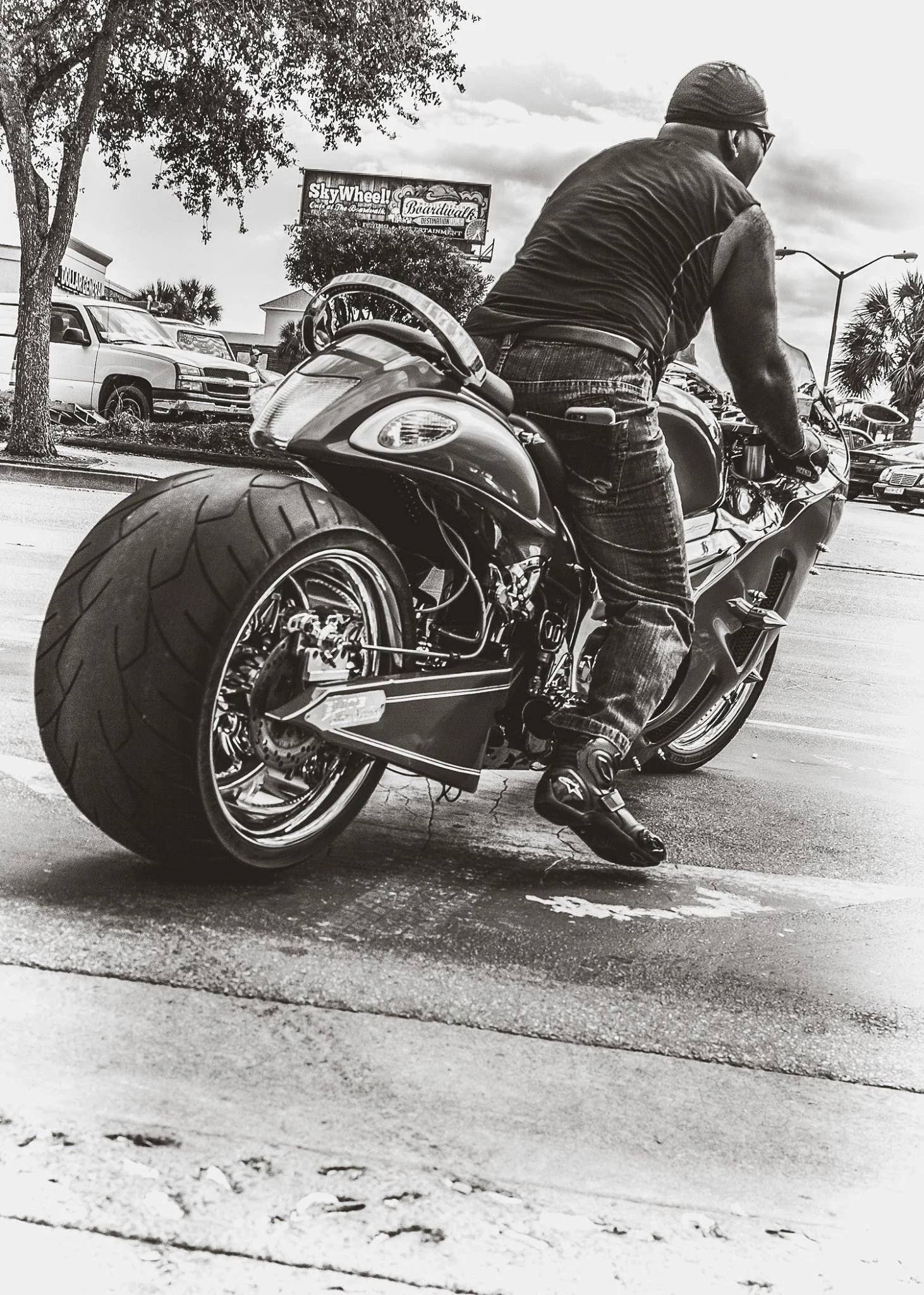 A man riding a sports motorcycle in a parking lot with cars and palm trees in the background, black and white photo.