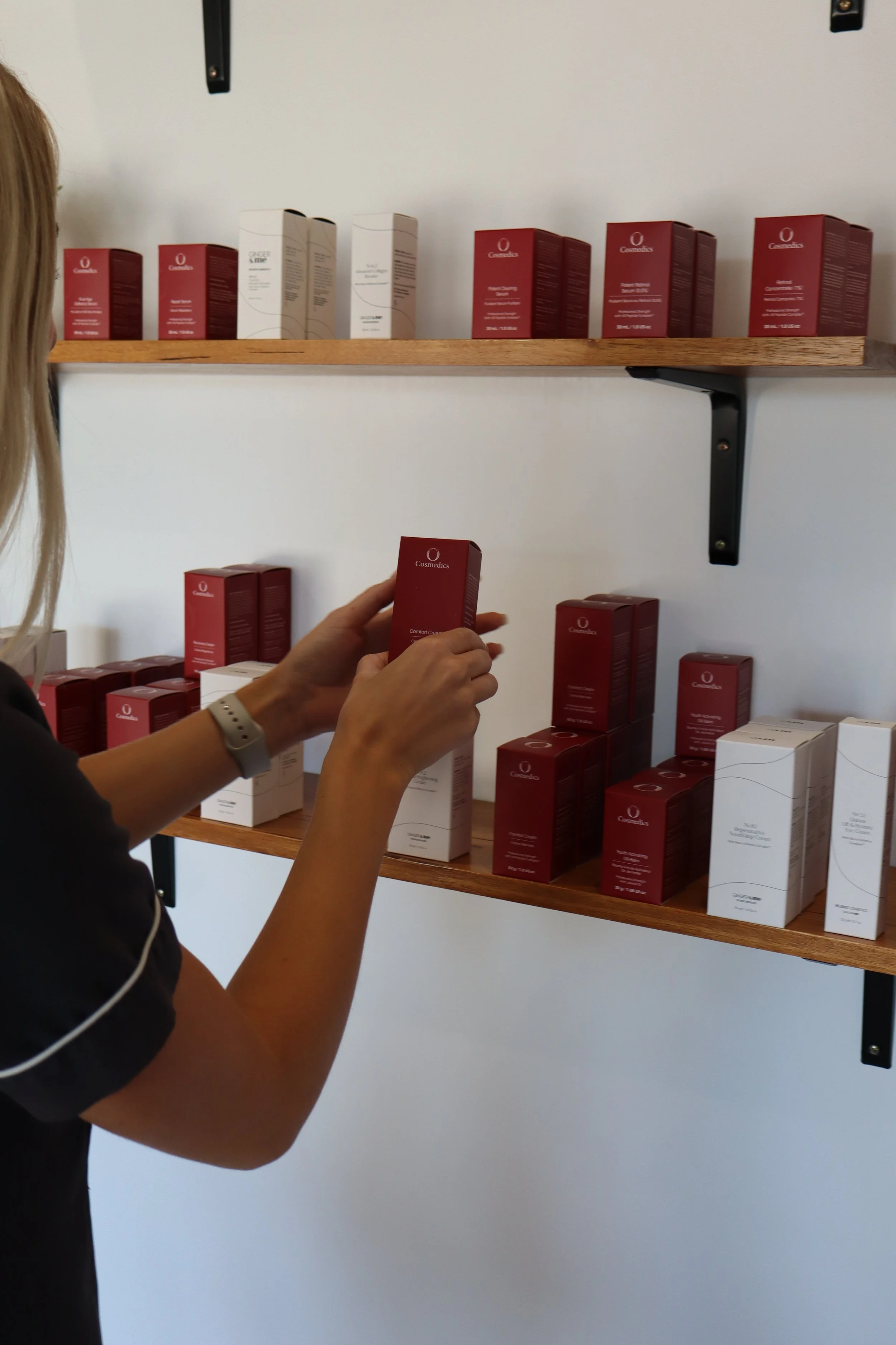 A woman shopping for skincare products on wooden shelves, holding a red box labeled 'Cosmedics' in a retail store.