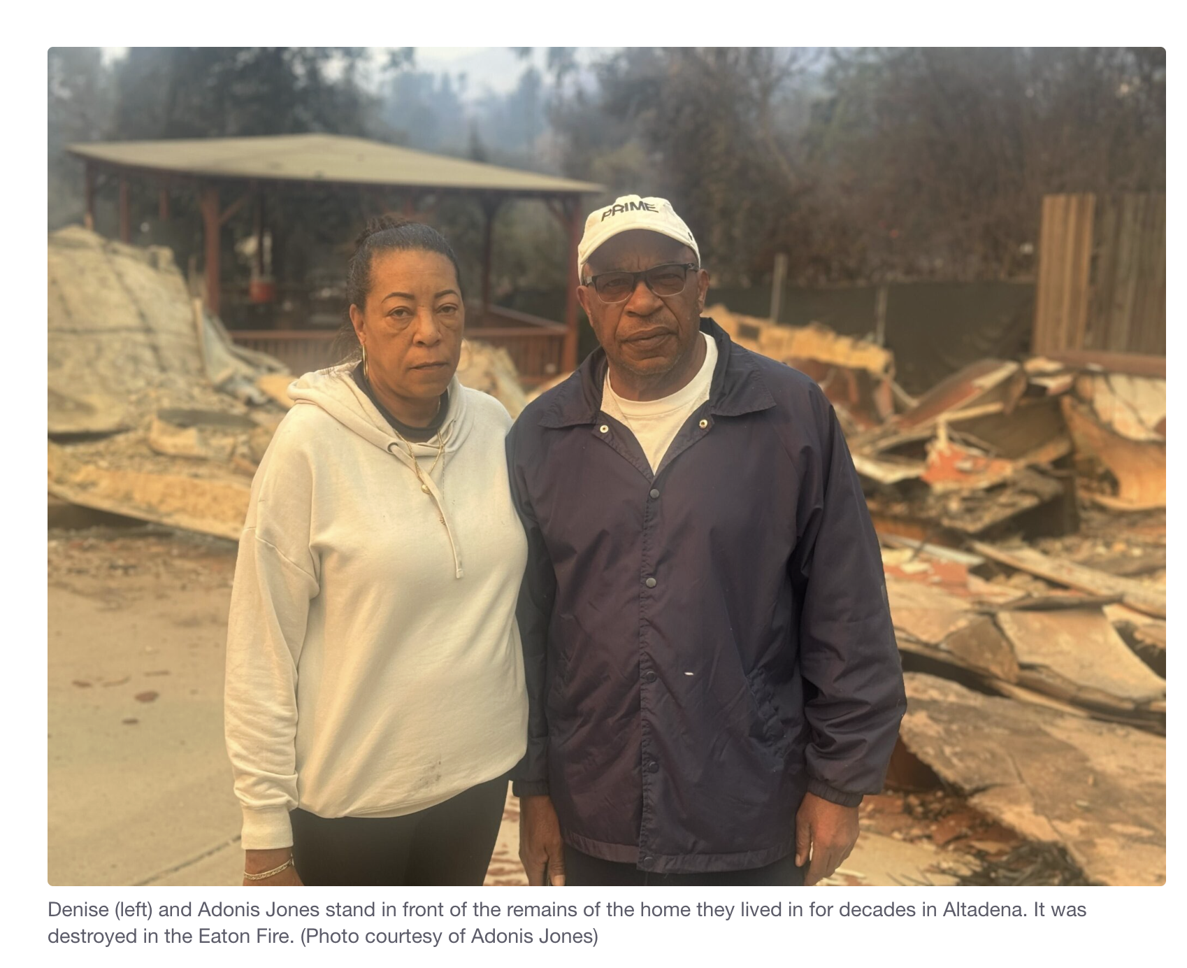 Denise and Adonis Jones standing in front of the remains of their home, with rubble and debris from the fire behind them.