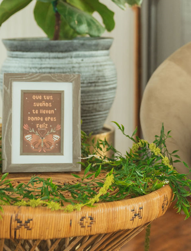 A decorative table with green foliage, a framed quote in Spanish, and a large potted plant behind it.