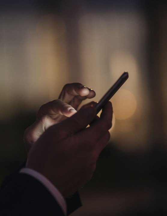 Close-up of a person’s hands holding and using a smartphone in a dimly lit environment.