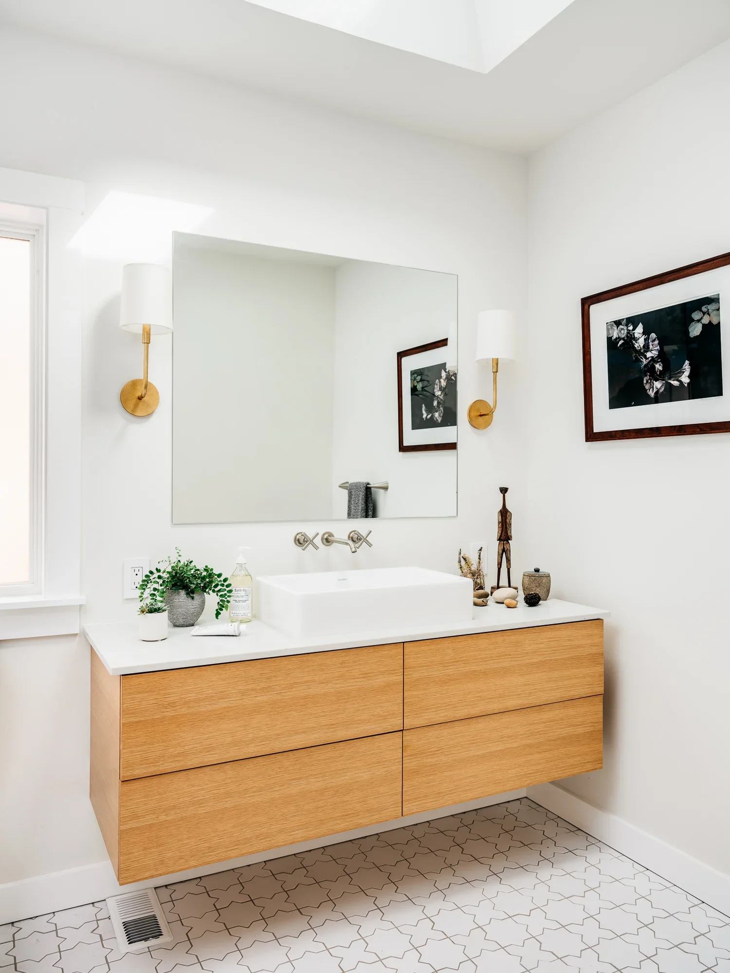 Modern bathroom vanity with floating natural oak cabinet, white vessel sink, brass wall sconces, and arabesque tile floor — spa-inspired bathroom remodel by Mokume Design Studio