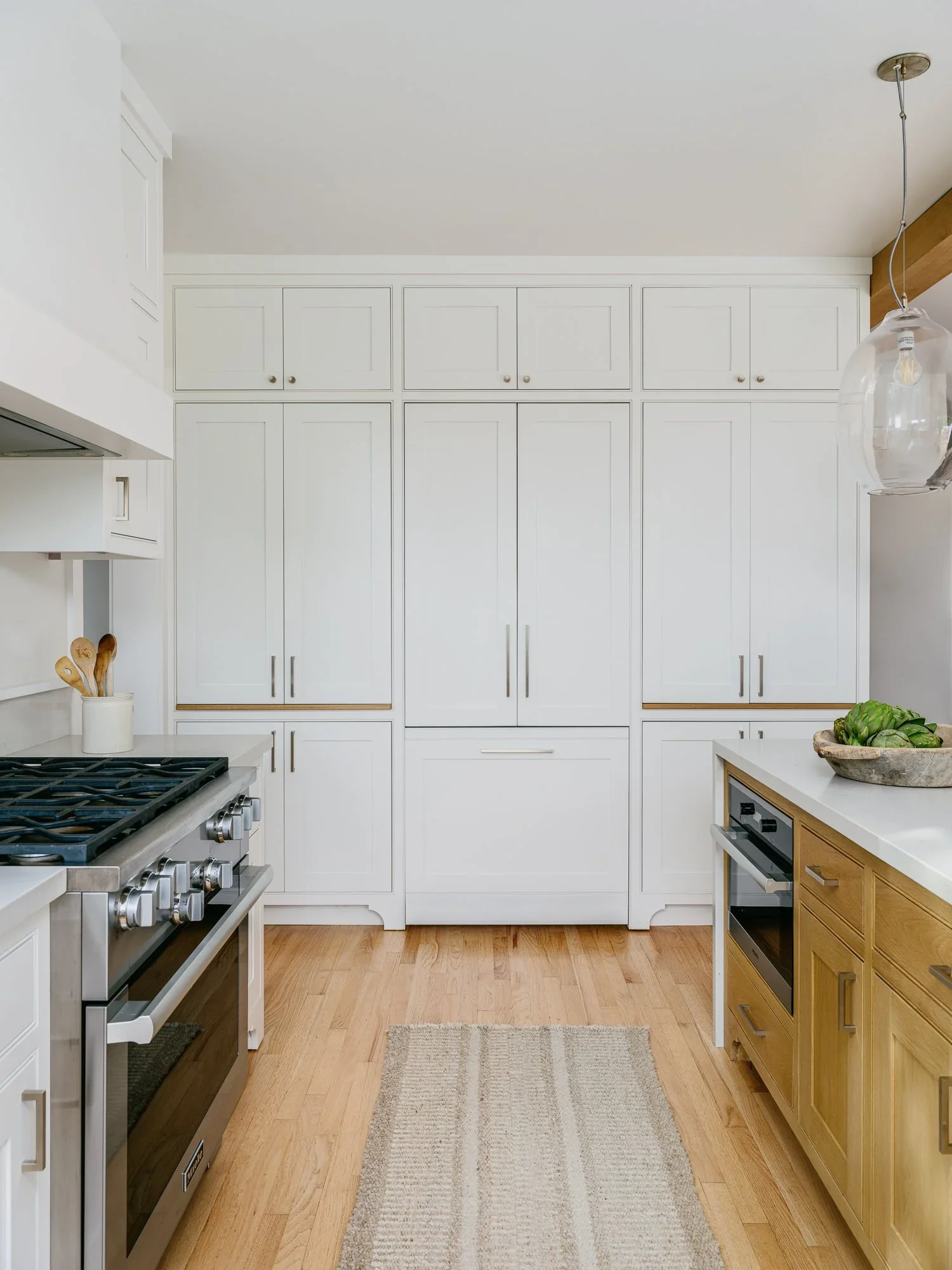 Floor-to-ceiling white shaker pantry cabinetry with integrated panel refrigerator, natural oak lower cabinets, and globe glass pendant — Kentfield California kitchen remodel by Mokume Design Studio